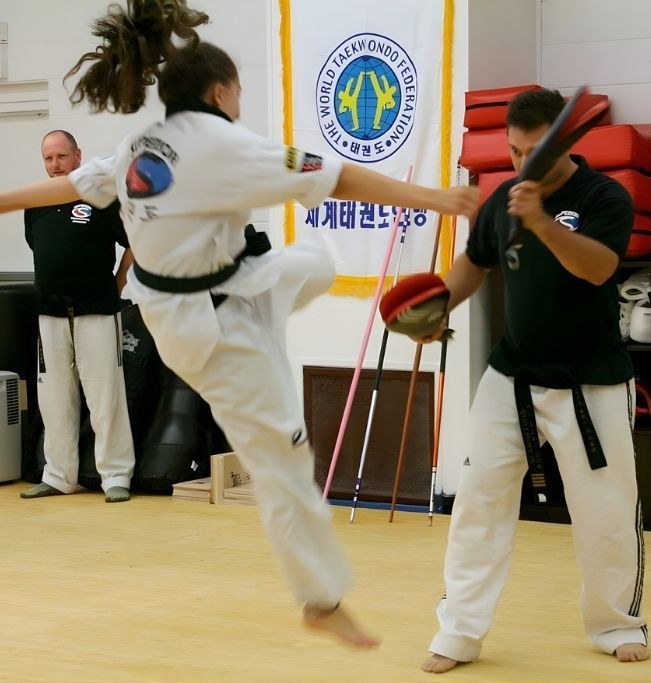 Five people in jiu-jitsu uniforms on a blue mat, including a man with a red belt, posing in a gym.