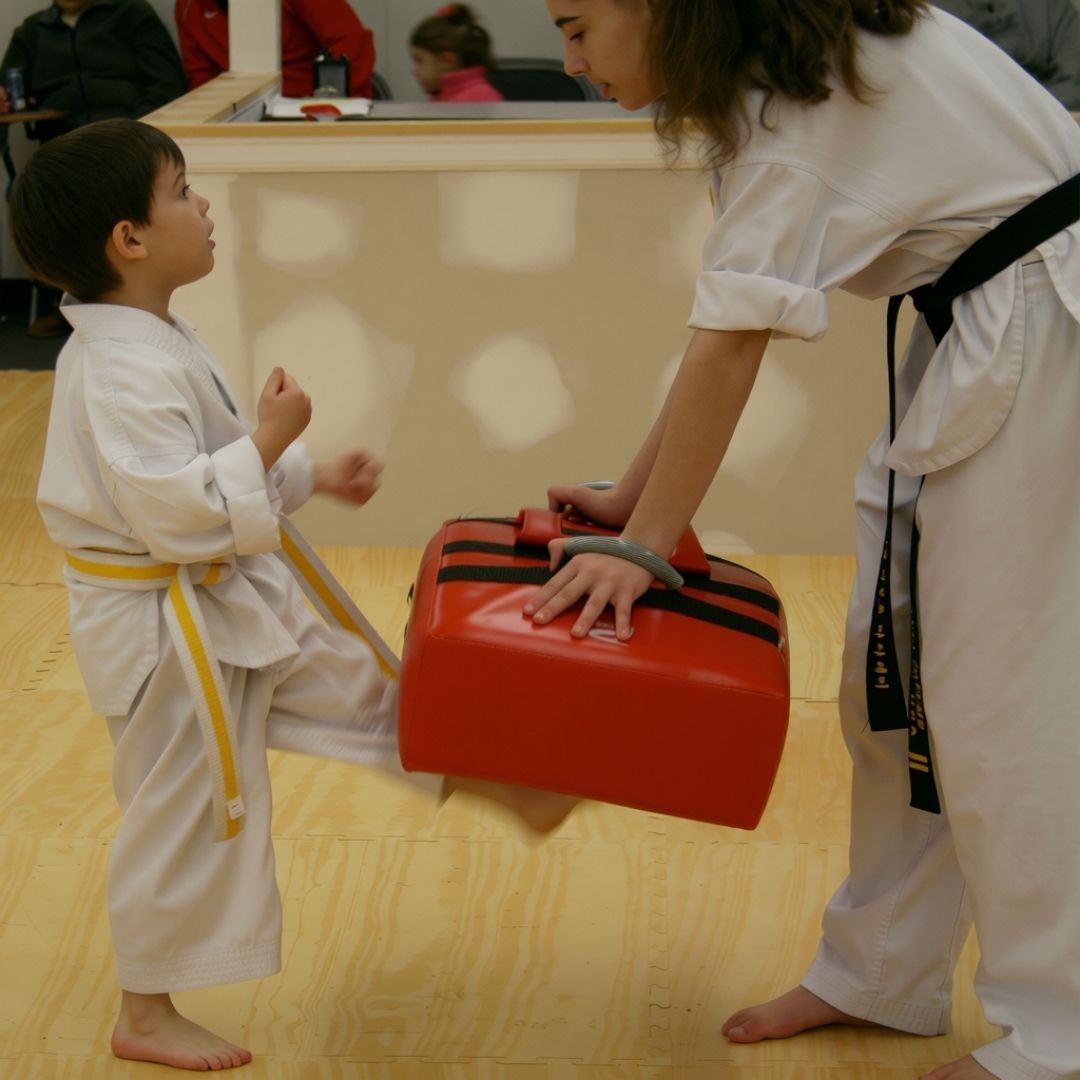 Two young children in blue and black martial arts uniforms grappling on a gym floor, one smiling.