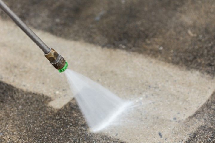 Pressure washer spraying water onto a concrete surface near a curb