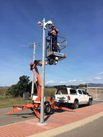 Man is Standing on Top of a Crane Working on a Street Light — Sape Industries in Garbutt, QLD
