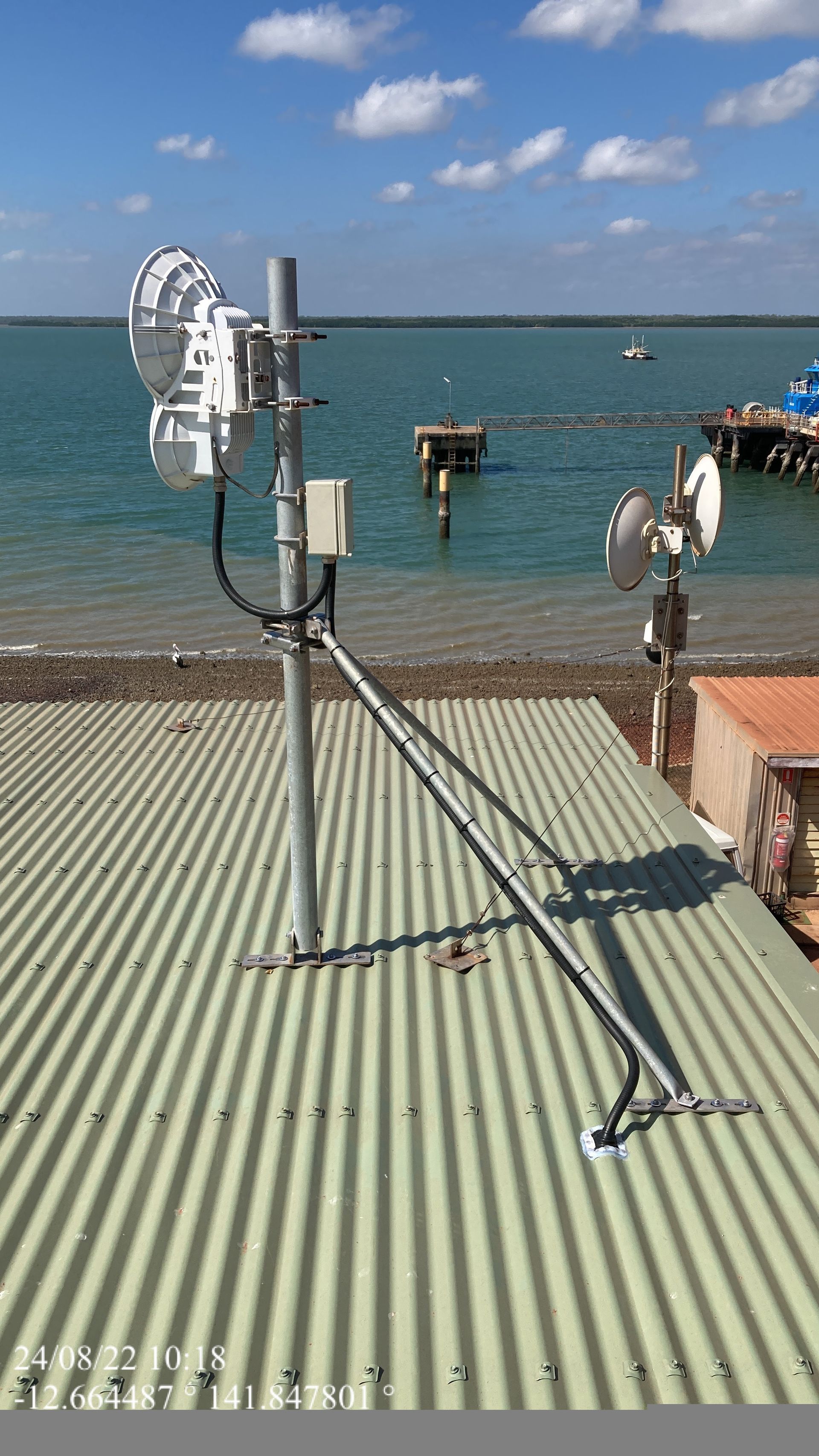 A satellite dish is sitting on top of a metal roof next to a body of water.
