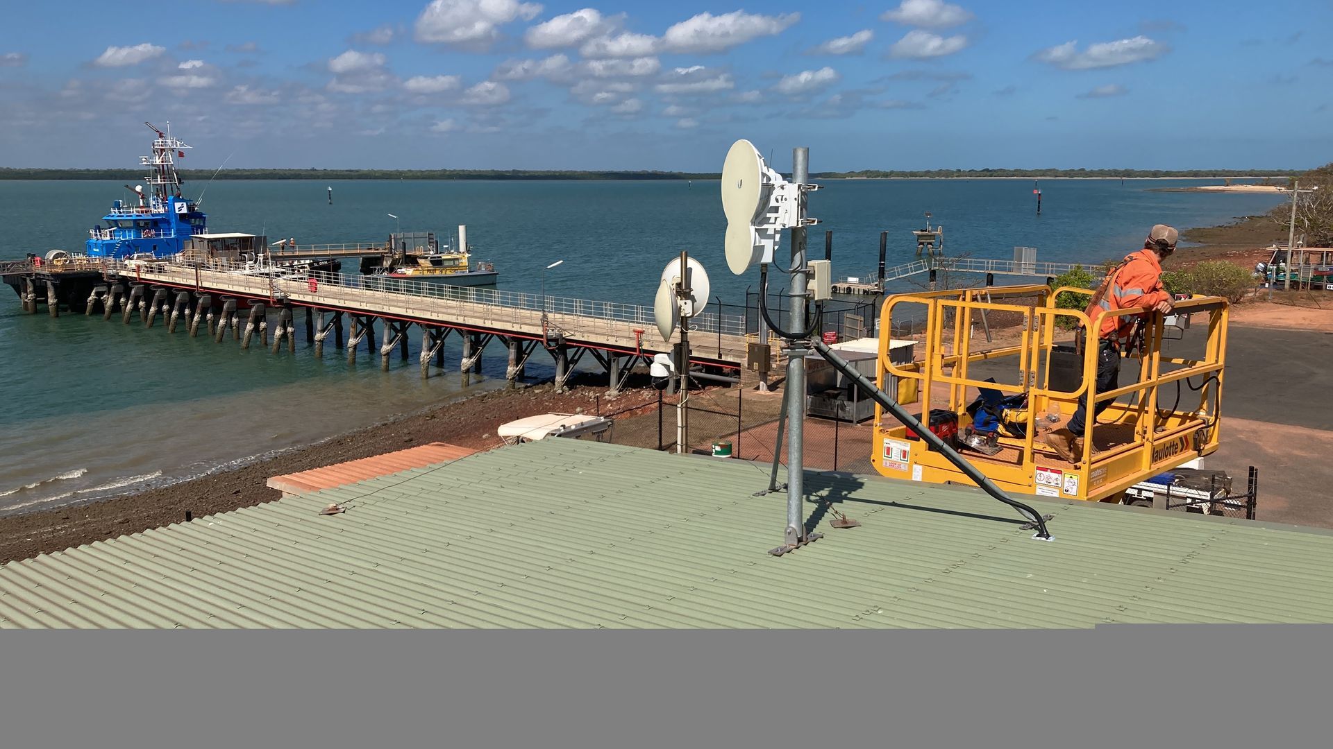 A man is sitting in a crane next to a pier overlooking the ocean.
