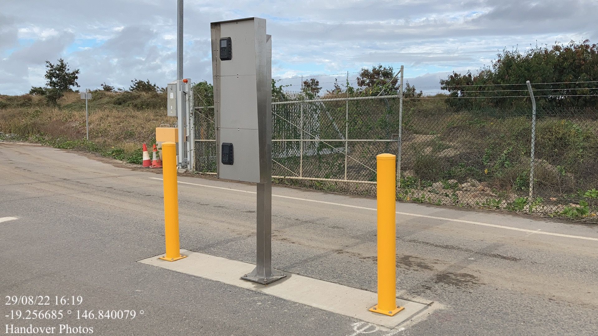 A parking meter is sitting on the side of the road next to two yellow poles.