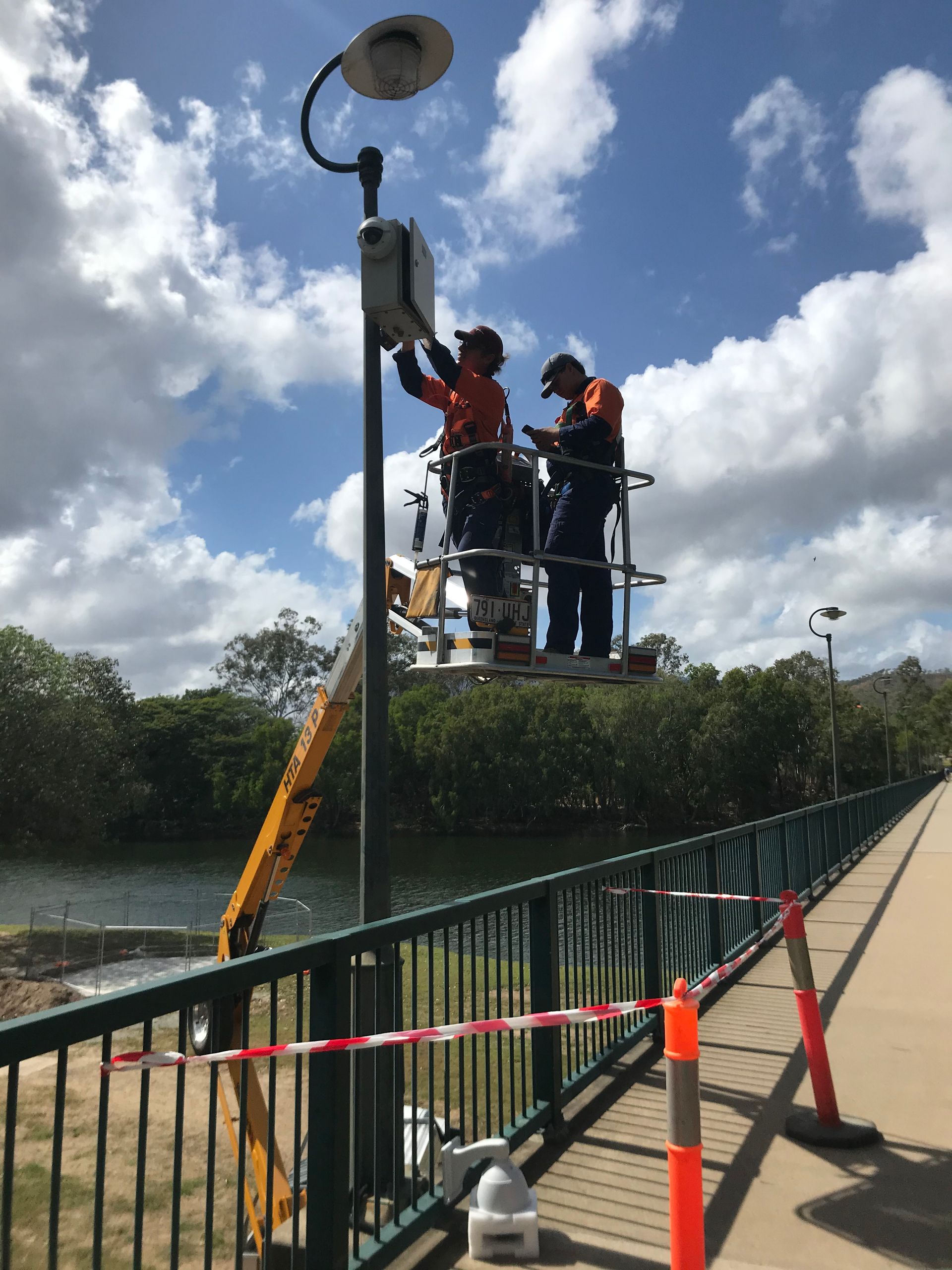 Two men are working on a street light on a bridge