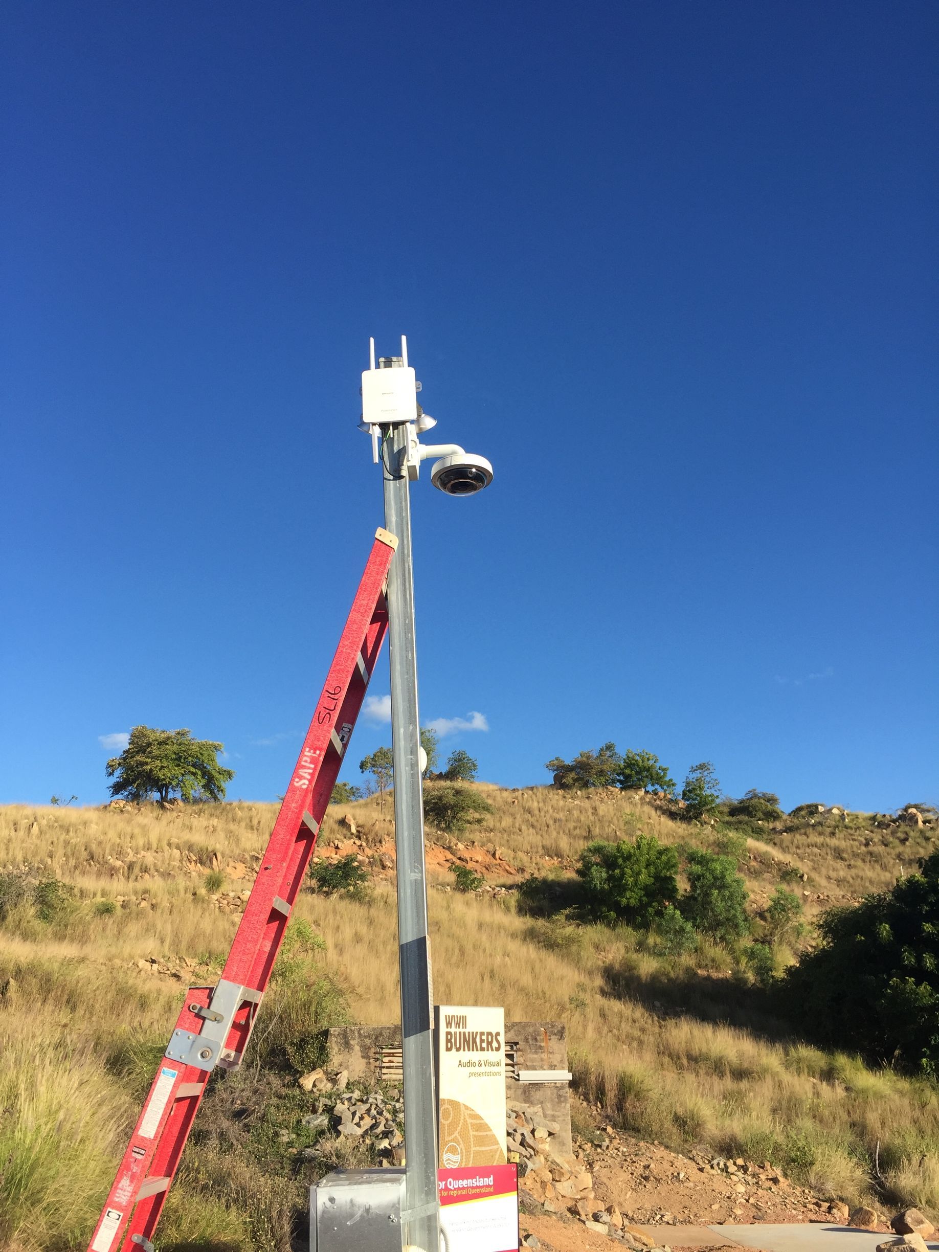 A red ladder is attached to a pole with a camera on it.