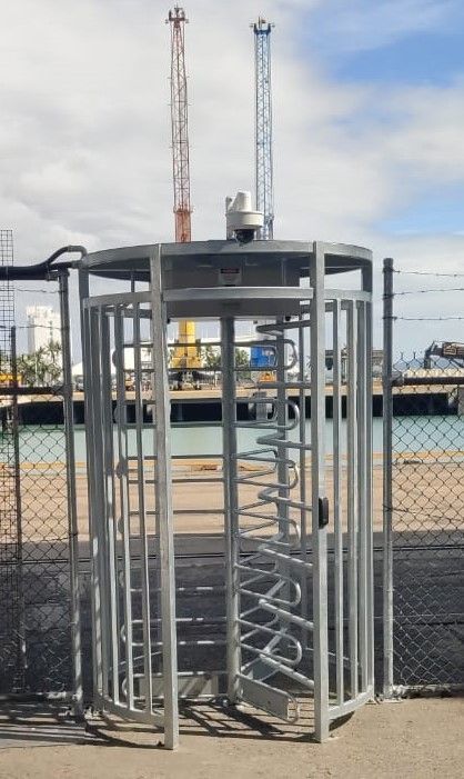 A metal gate with a camera on top of it is surrounded by a chain link fence.