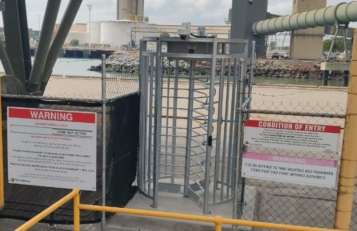A warning sign is next to a turnstile in a fenced in area.