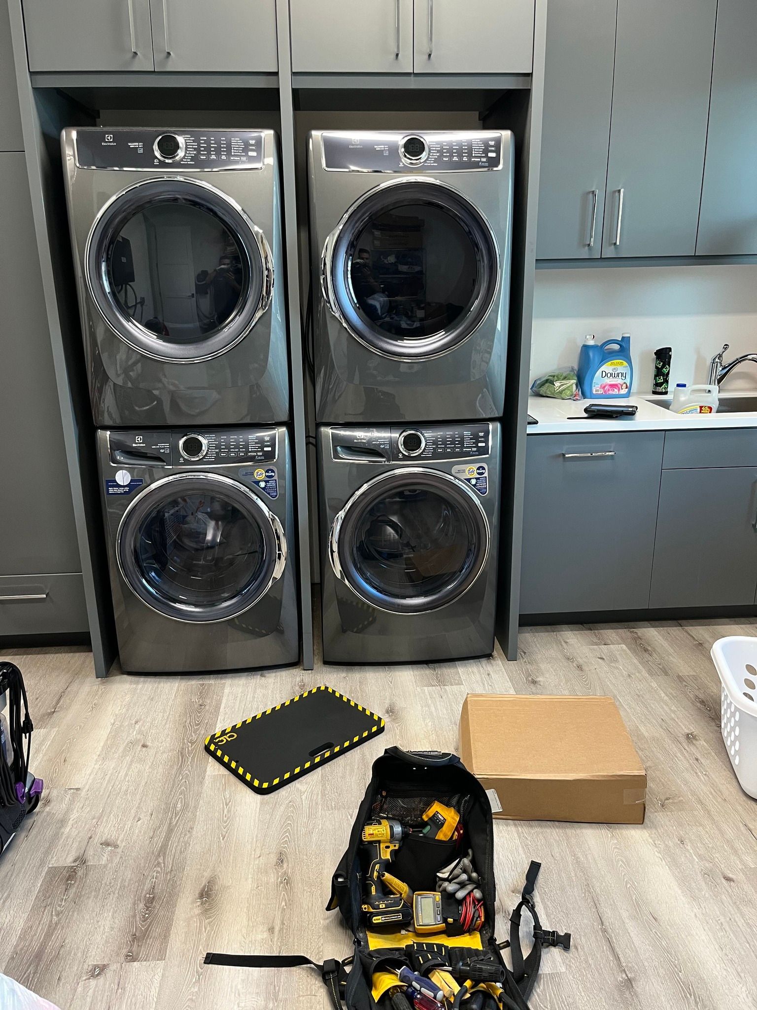 Four gray washing machines in a laundry room, tools and box in front.