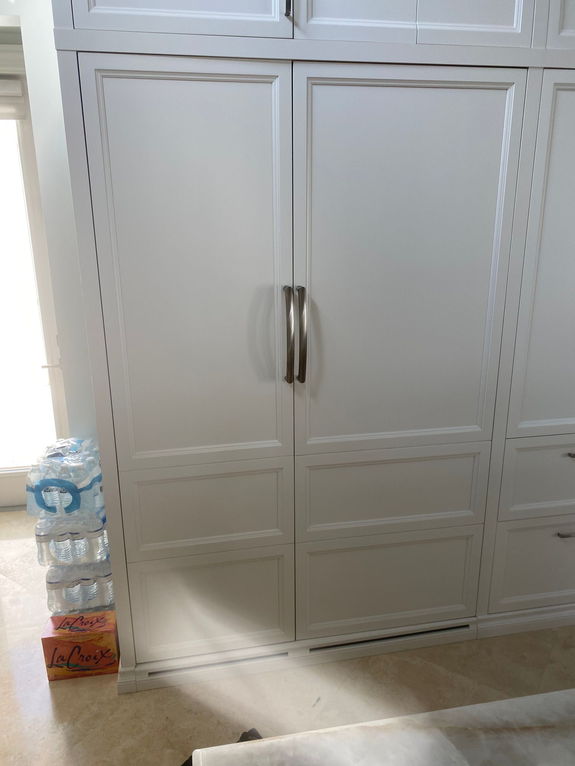 White closet with silver handle, drawers below, and stacked water bottles to the left.
