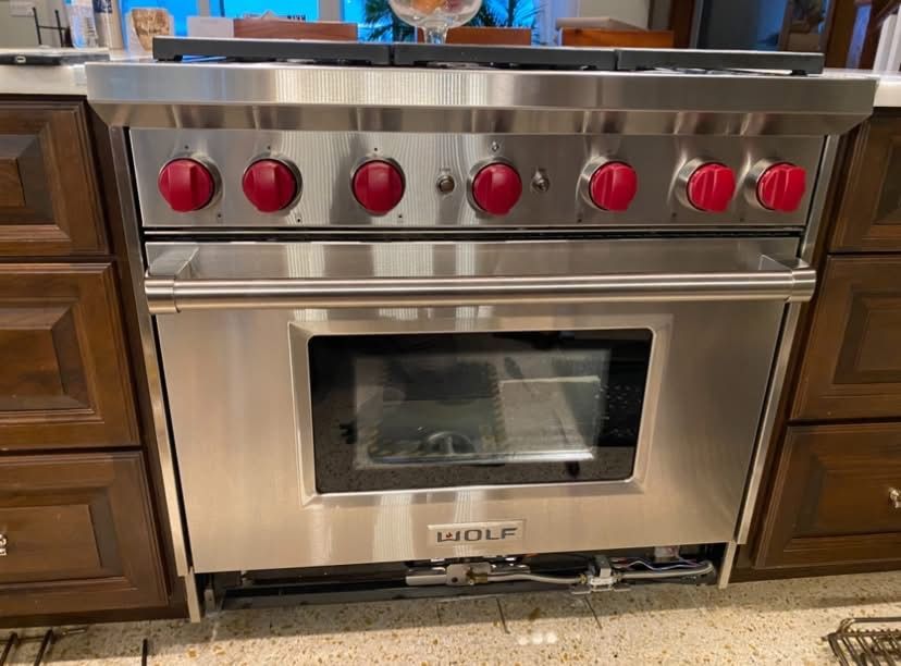 Stainless steel Wolf range with red knobs, installed in a wooden cabinet.