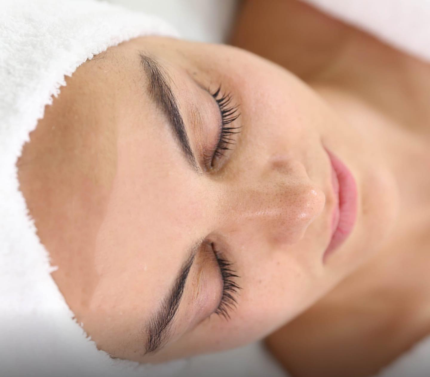 Frau mit Handtuch um den Kopf und geschlossenen Augen bei einer Gesichtsbehandlung