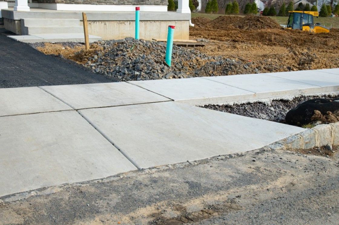 Newly poured concrete sidewalk, construction site, with a step up to a house entrance.