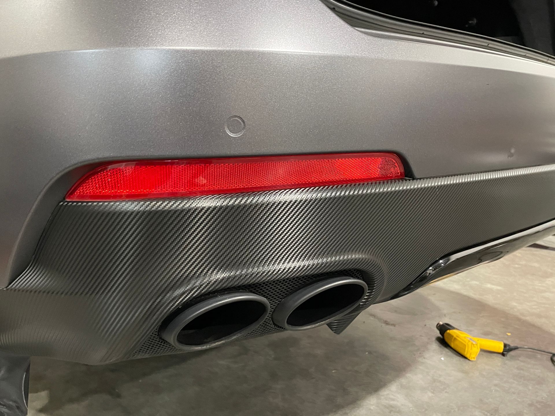 The rear end of a car is being wrapped in carbon fiber.