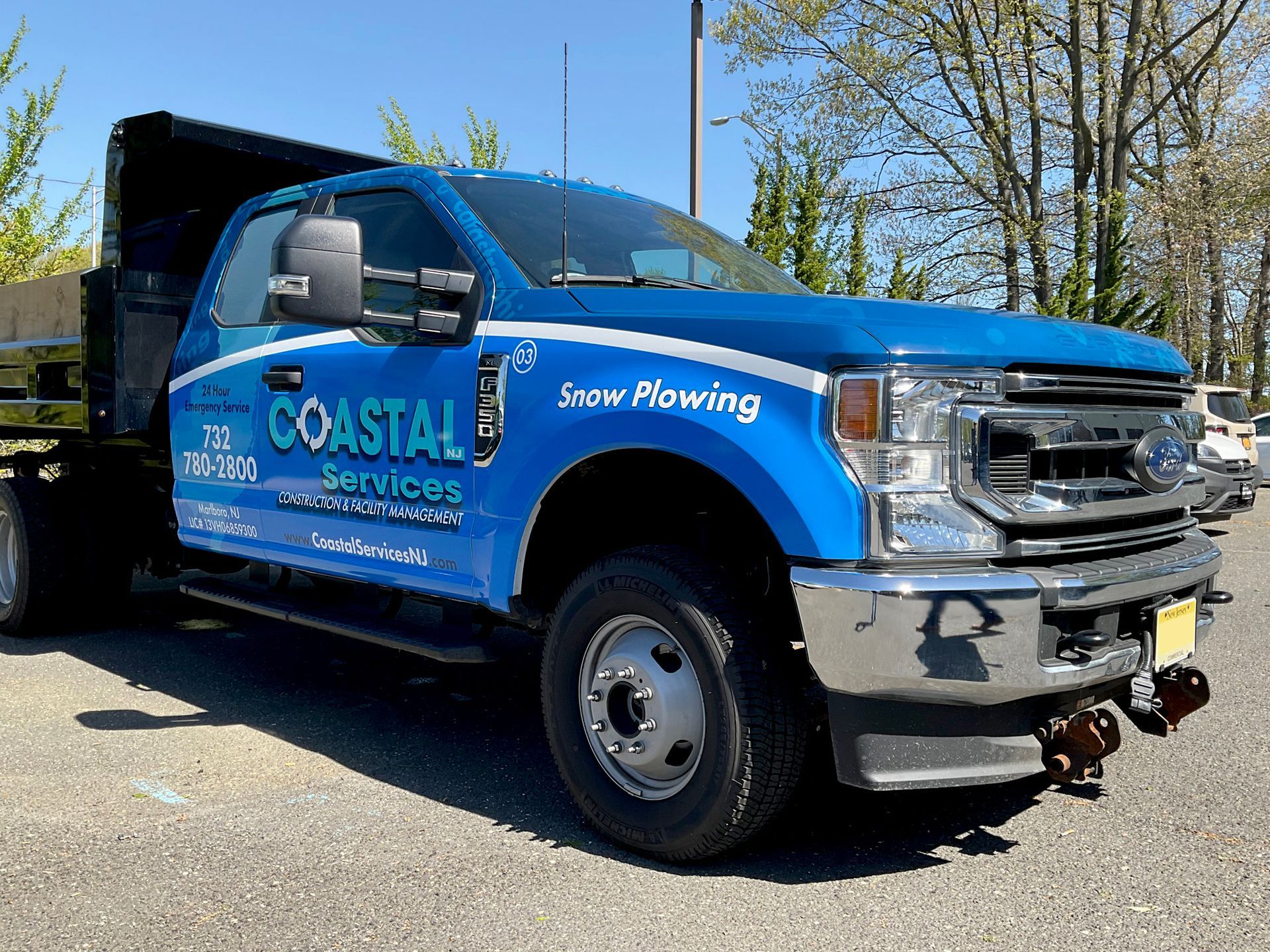 A blue coastal snow plowing truck is parked in a parking lot.