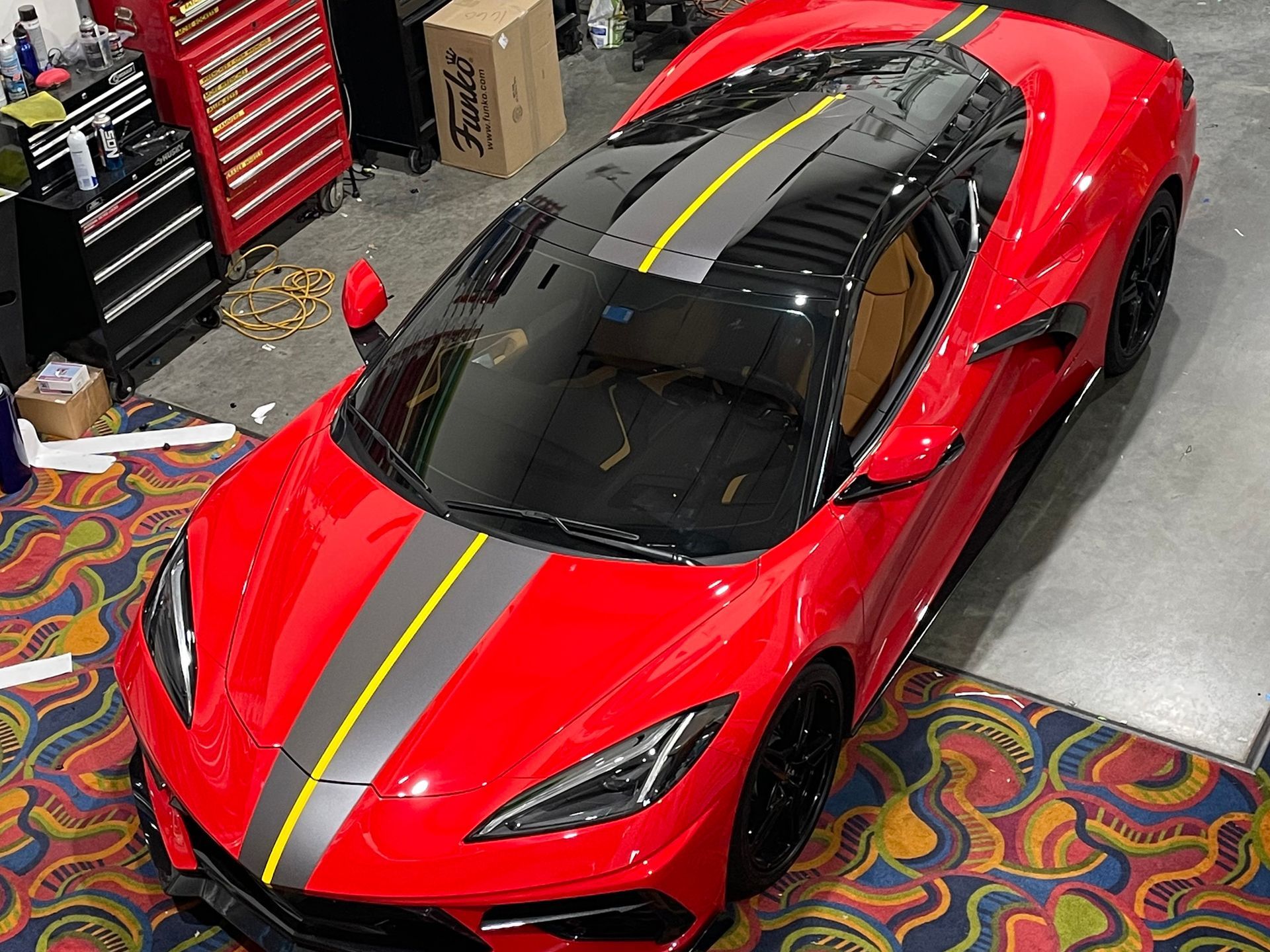 A red sports car with a black roof is parked in a garage.