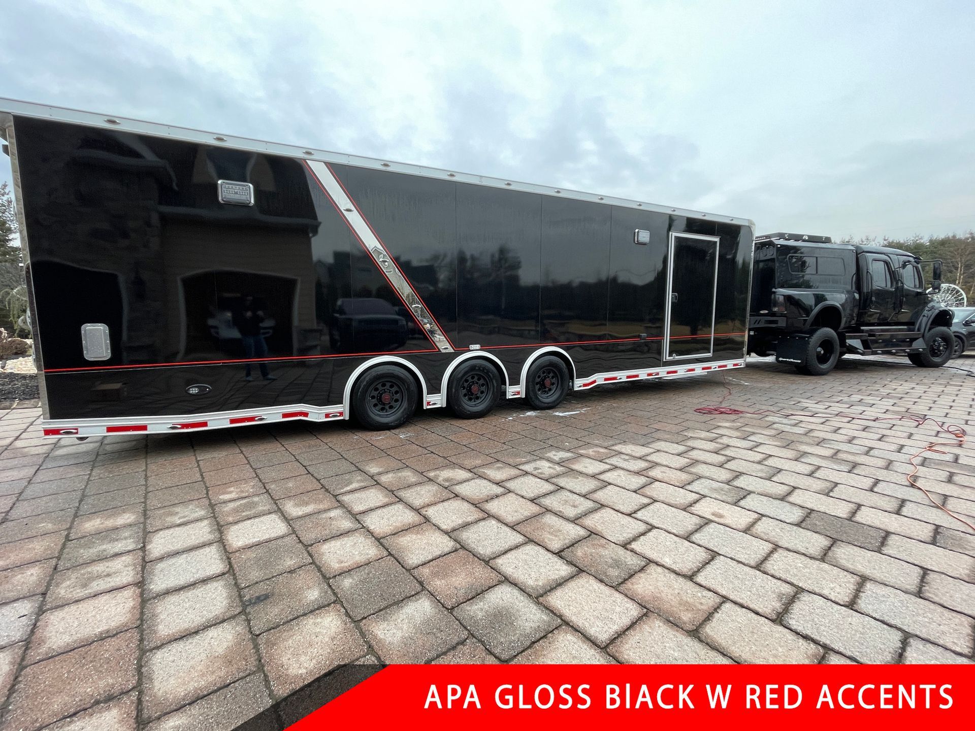 A black trailer is parked on a brick driveway next to a truck.