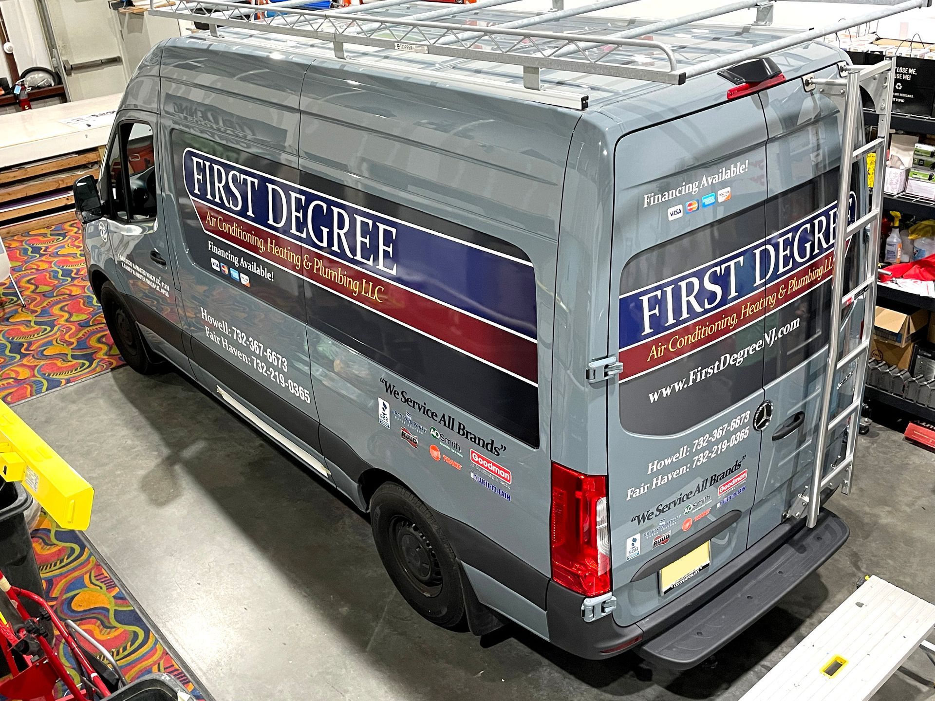 A gray van with a ladder on the back is parked in a garage.