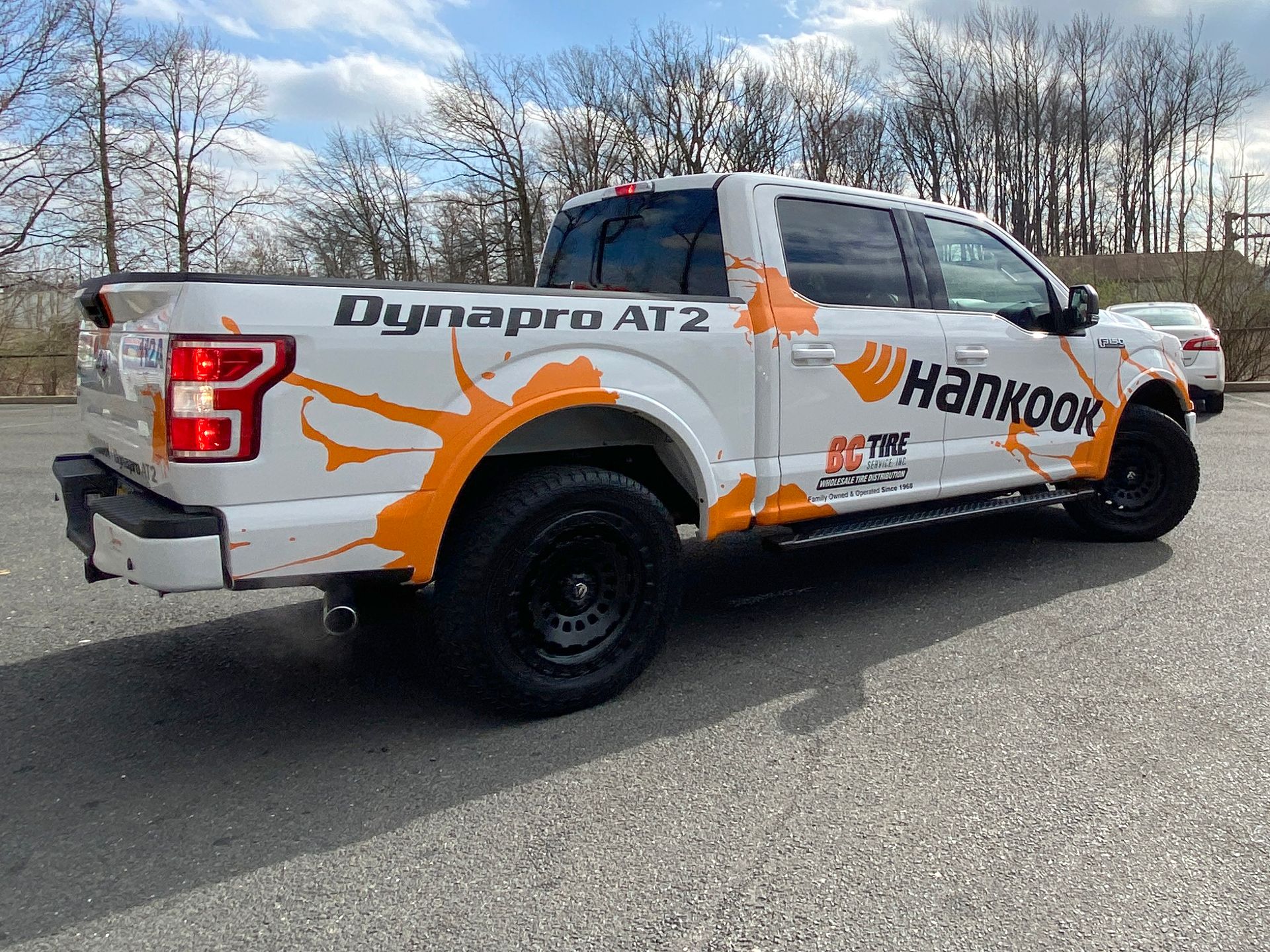 A white truck with orange graphics on it is parked on the side of the road.