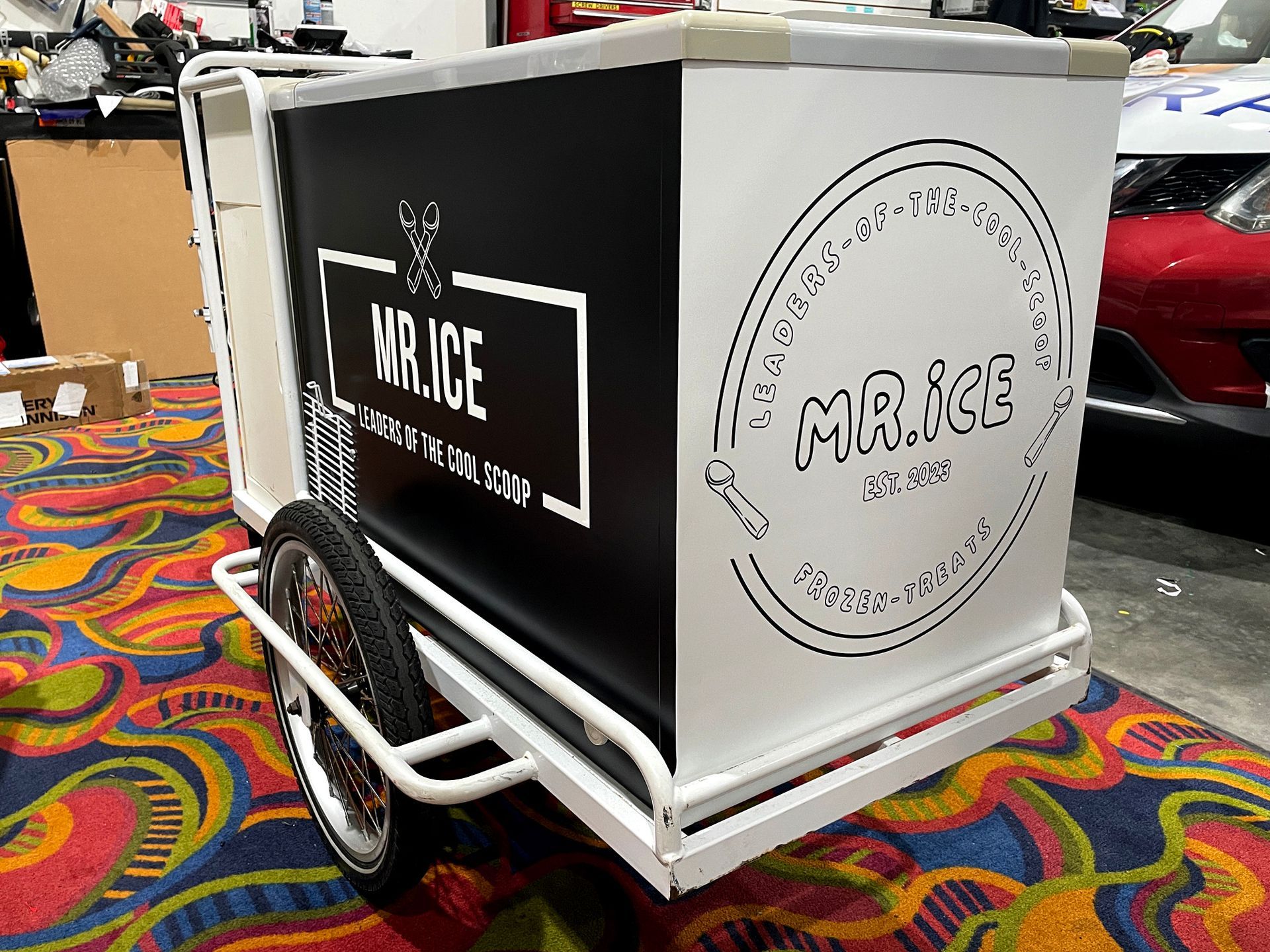A black and white ice cream cart is sitting on a colorful rug.