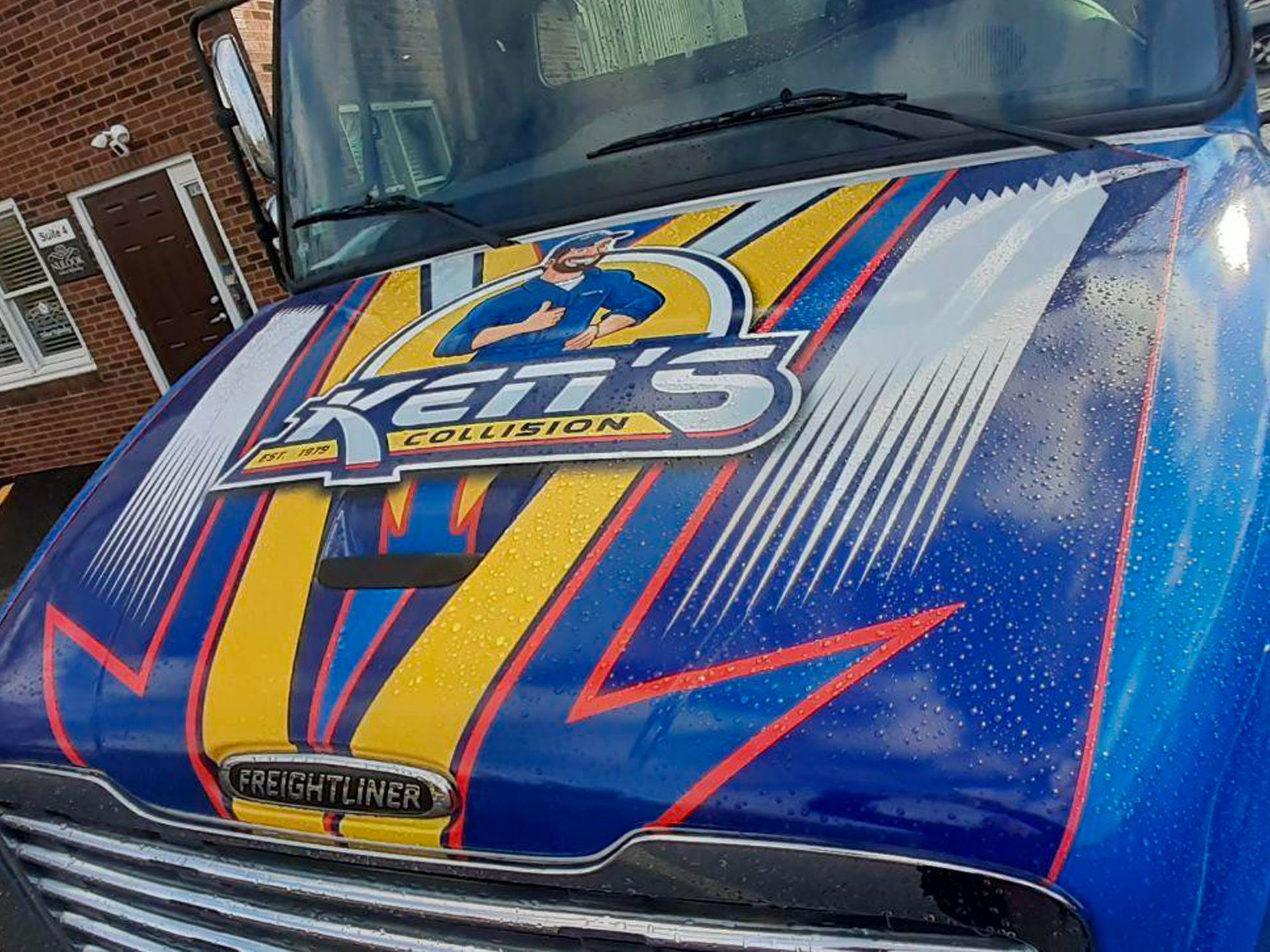 A blue truck with a ken 's collision logo on the hood