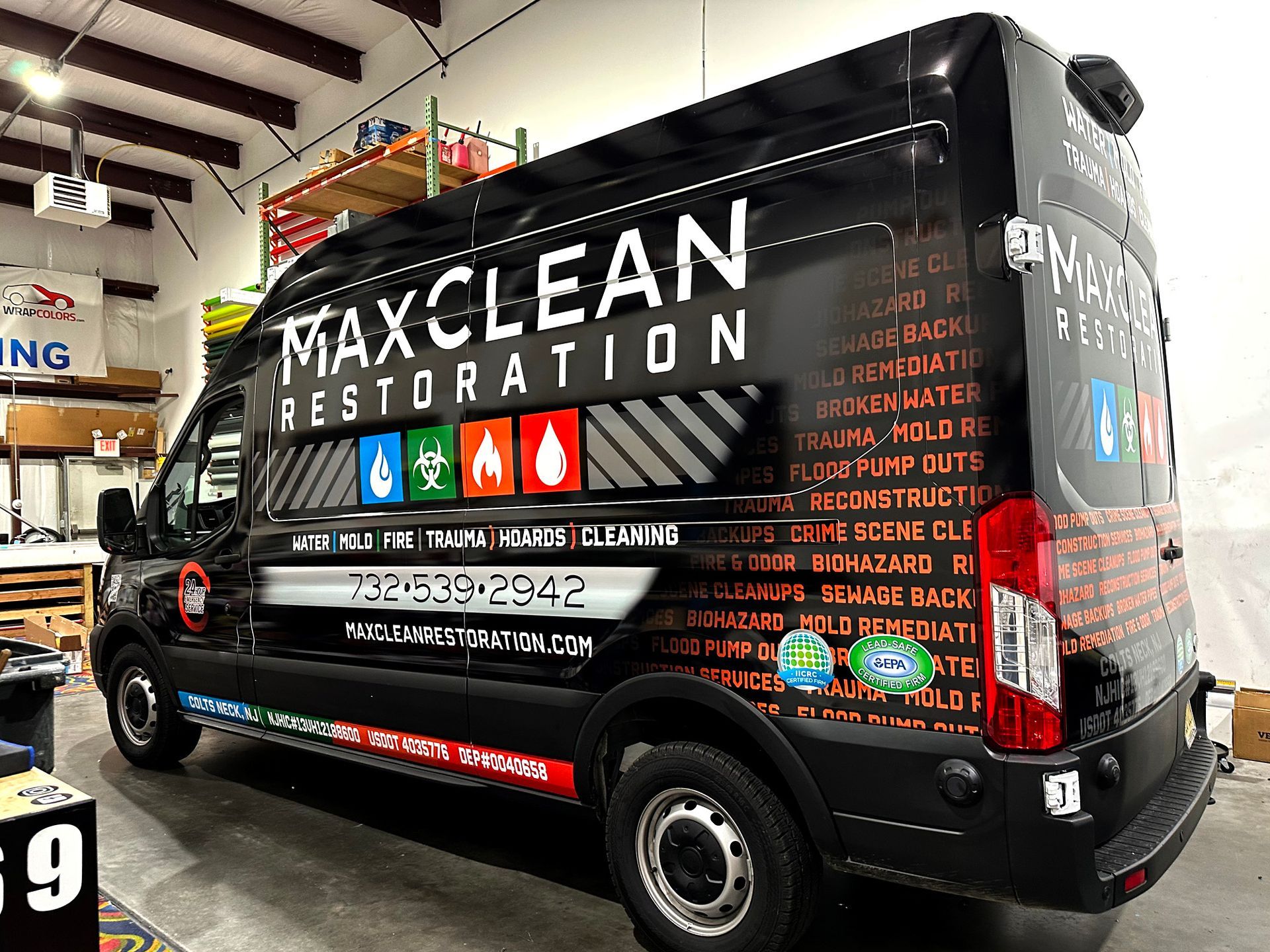 A black van with a wrap on it is parked in a garage.