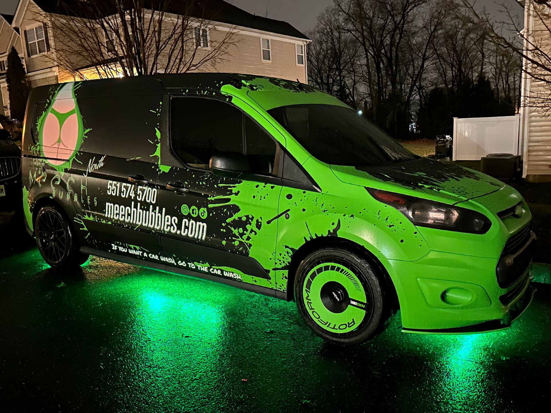 A green van is parked in front of a house at night.