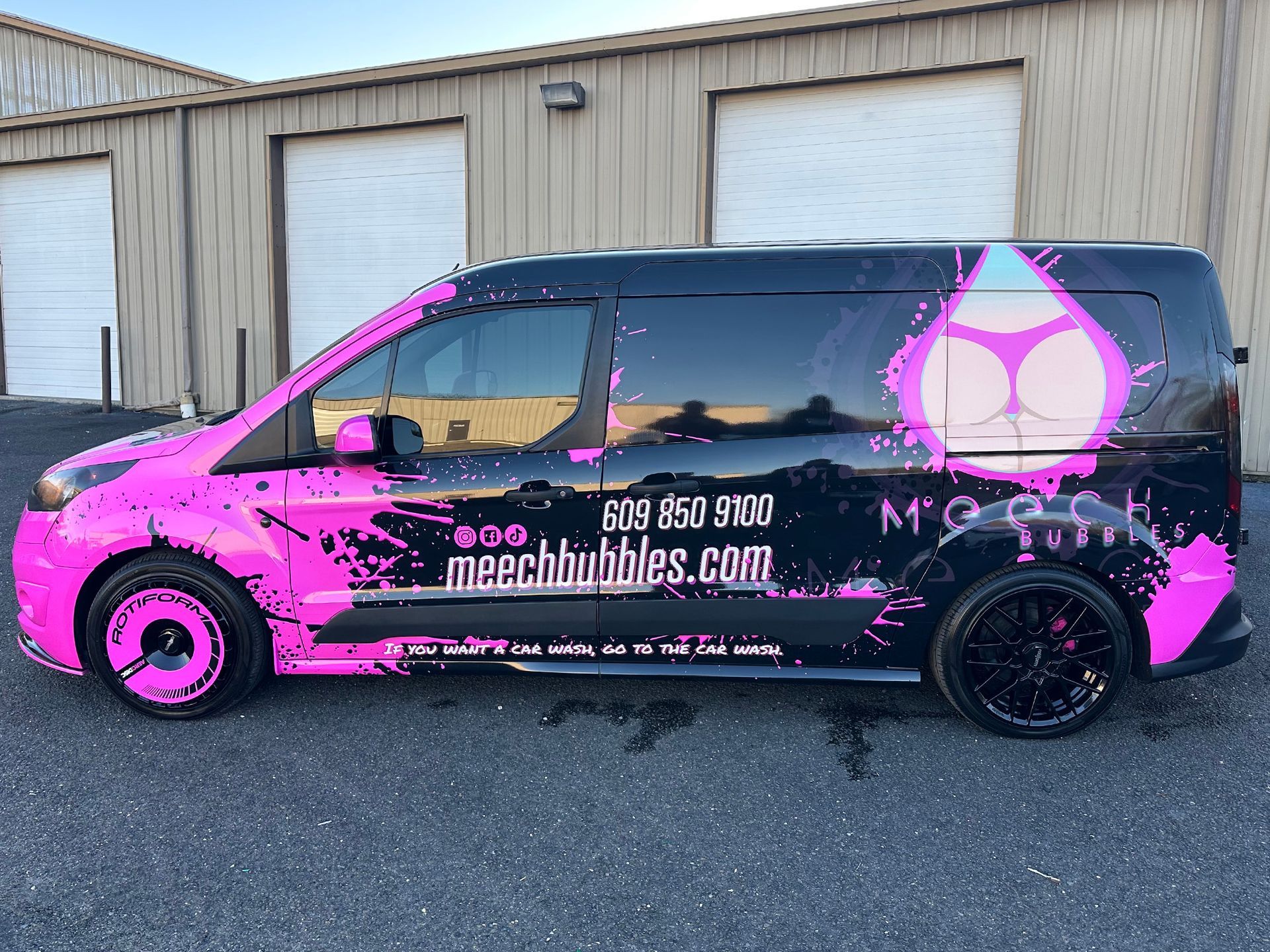 A pink and black van is parked in front of a building.