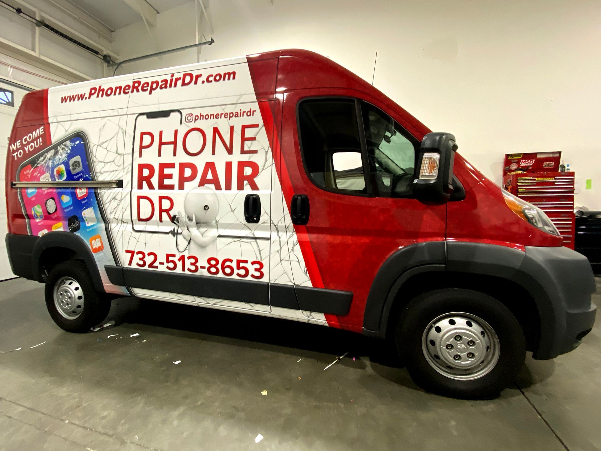 A red van with a phone repair dr. advertisement on the side is parked in a garage.