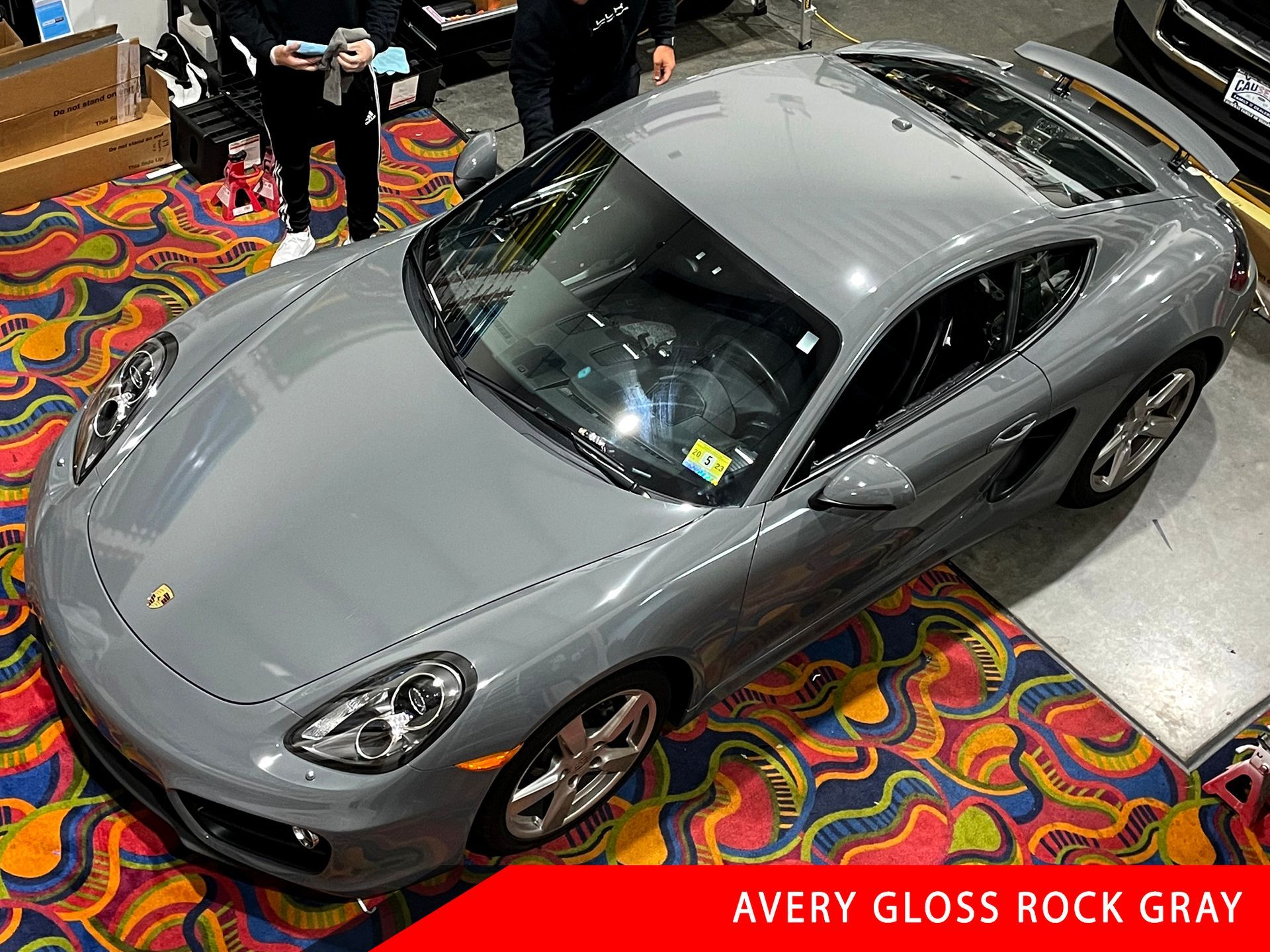 A grey sports car is sitting on a colorful carpet.