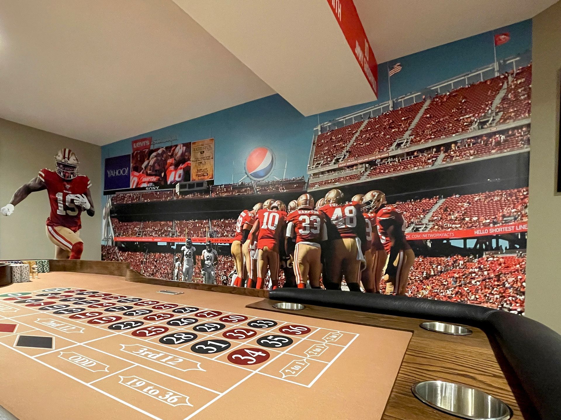 A roulette table with a picture of a football player on the wall behind it.