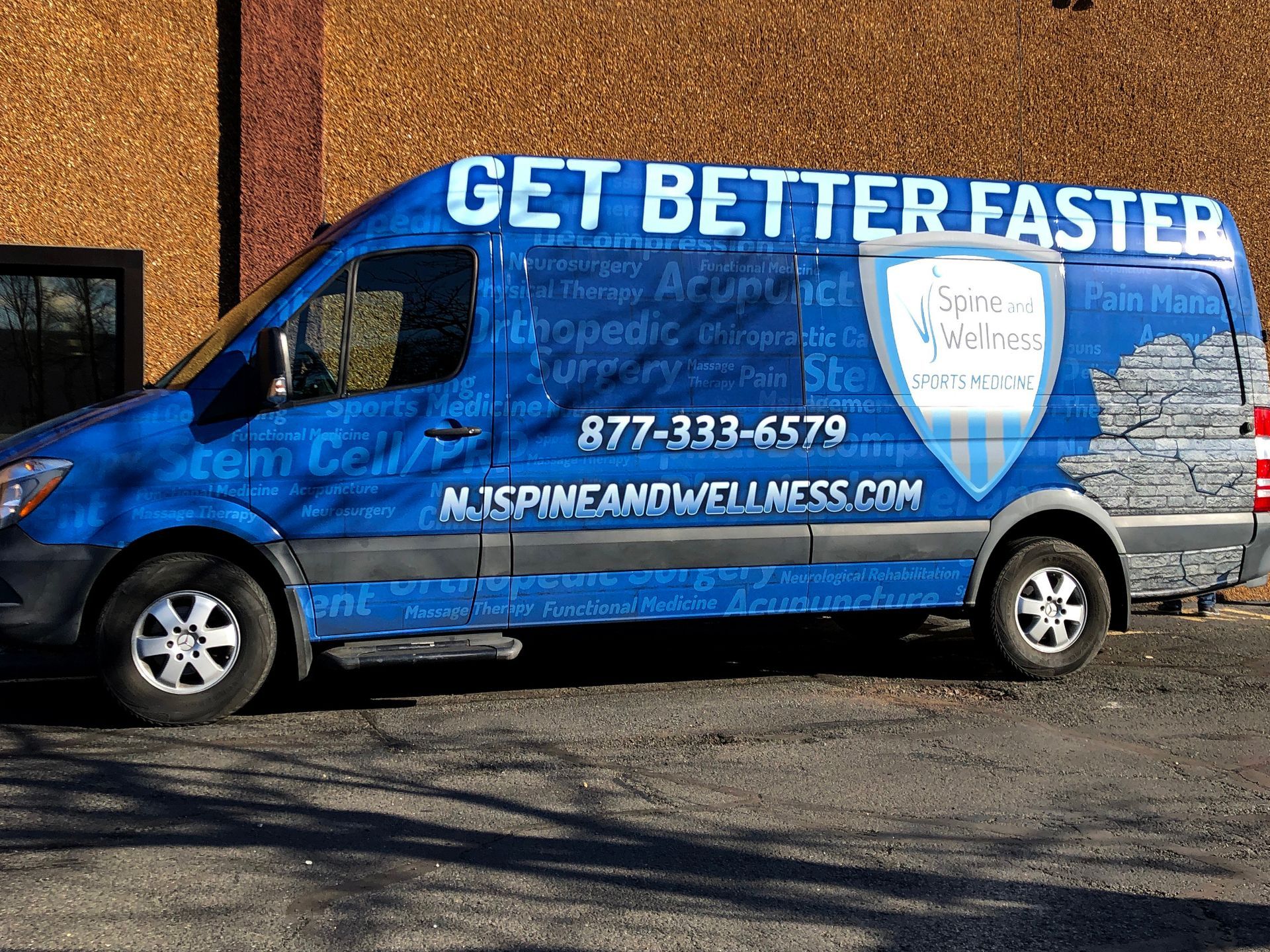 A blue van that says get better faster is parked in front of a building.