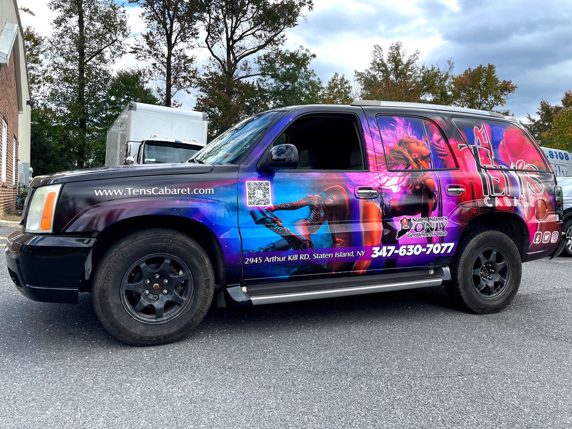 A black suv with a colorful wrap is parked on the side of the road.