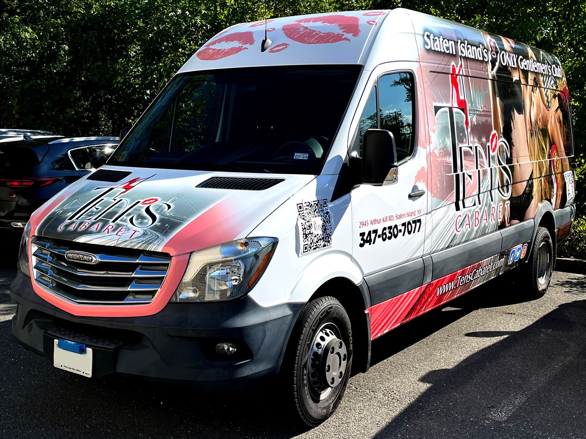 A white and red van with a kiss on the side is parked on the side of the road.