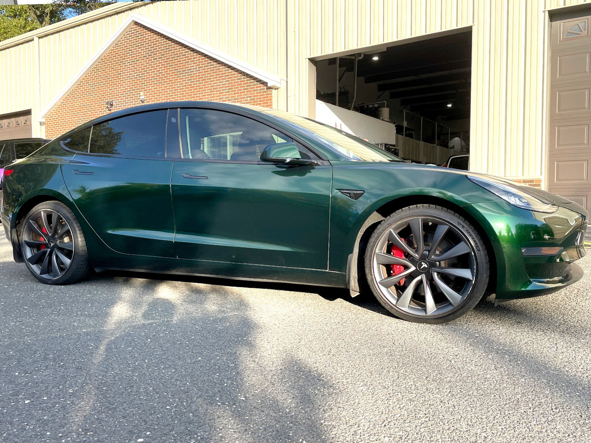 A green tesla model 3 is parked in front of a garage.
