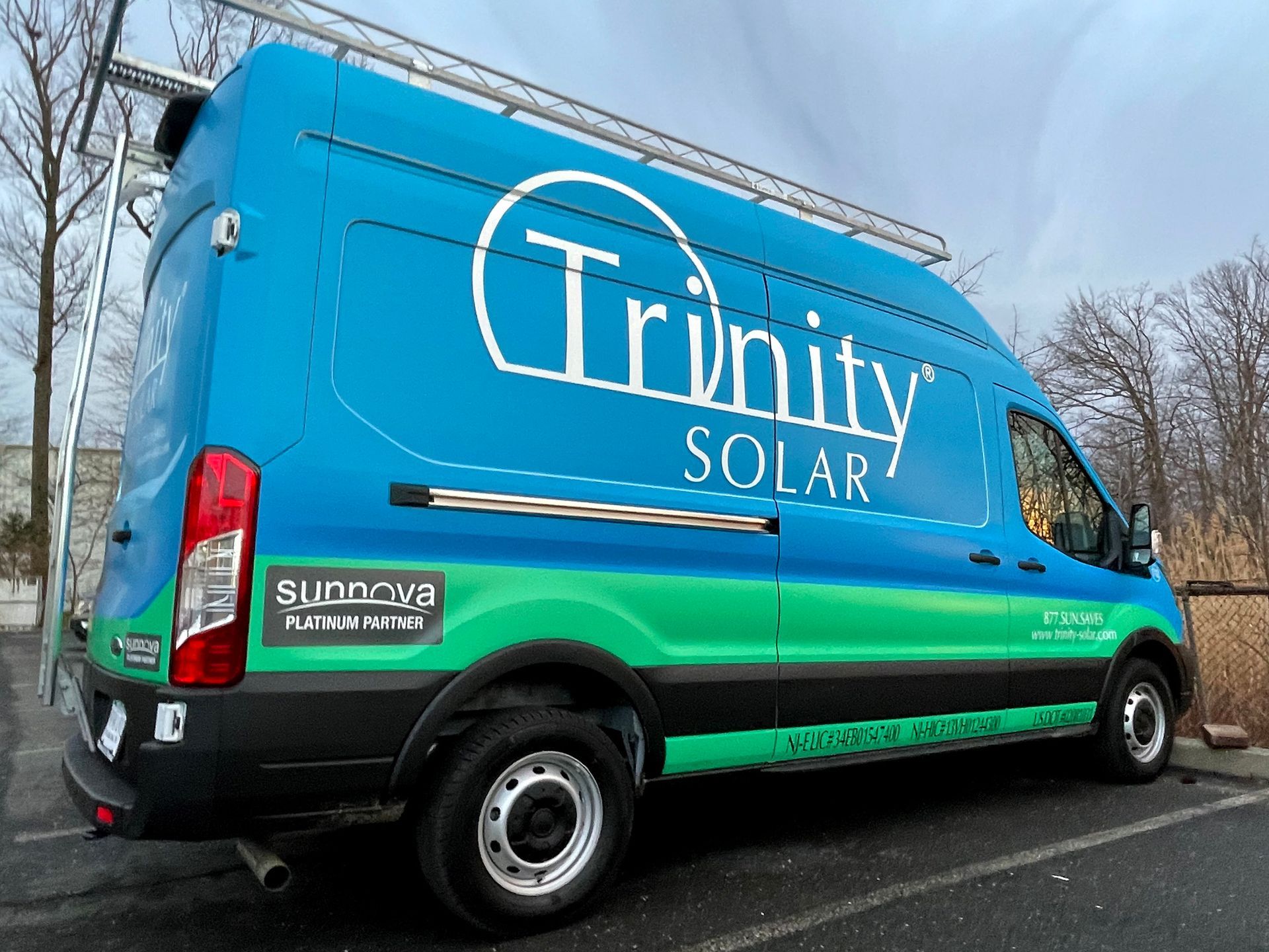 A blue and green van with trinity solar written on the side is parked on the side of the road.