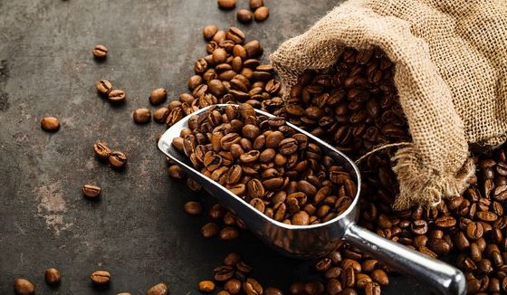 A bag of coffee beans spilled out on a table with a filled scoop nearby