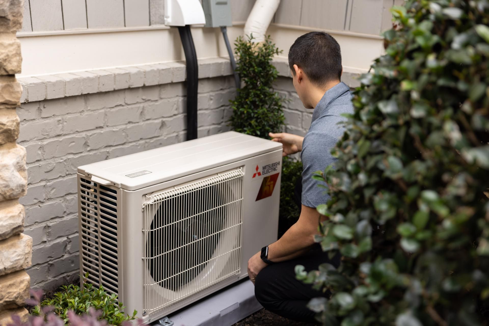 Man in blue shirt and cap inspecting a ceiling air vent, pointing at it.