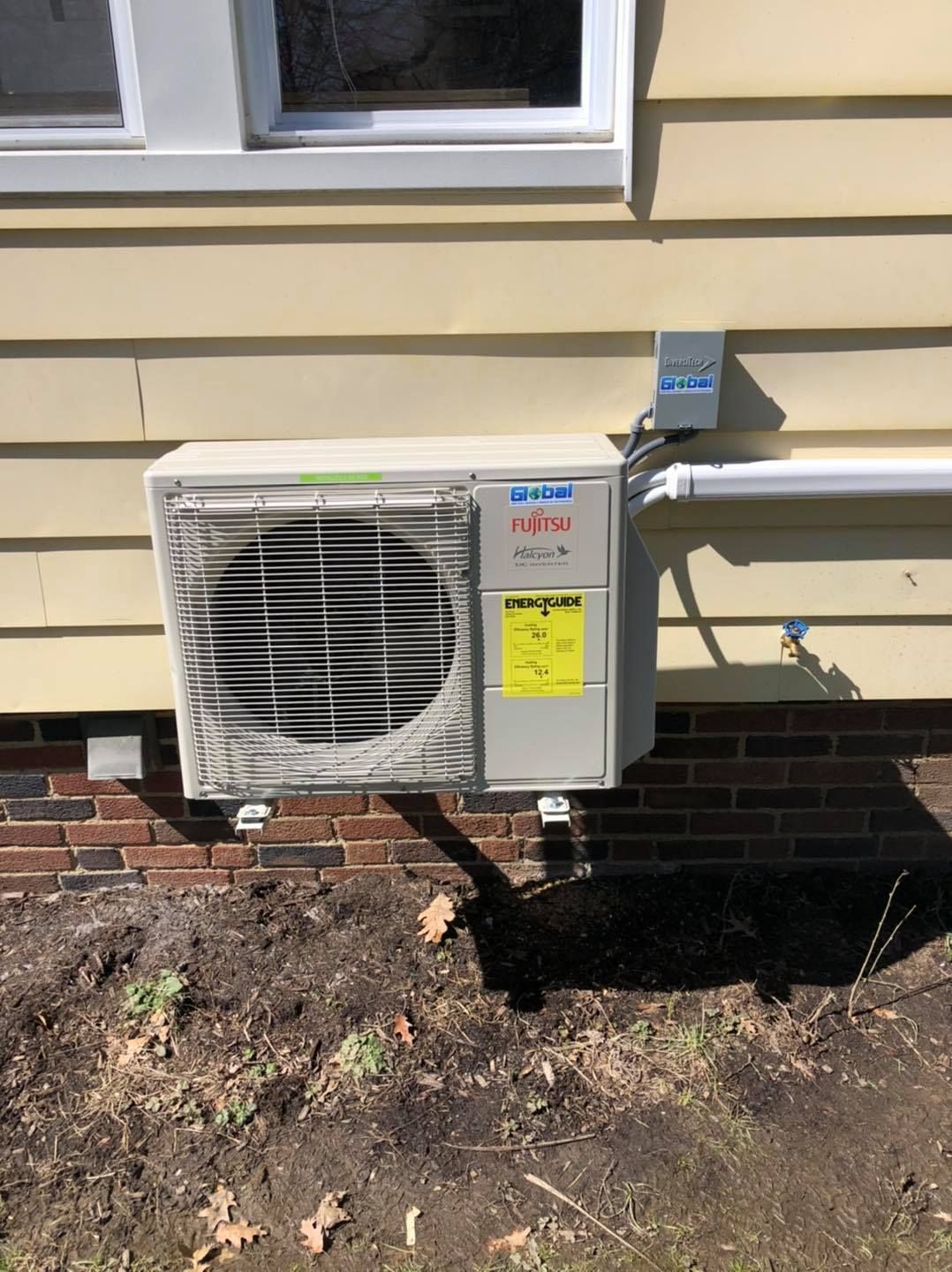 Fujitsu heat pump mounted on a brick and siding wall with electrical components.
