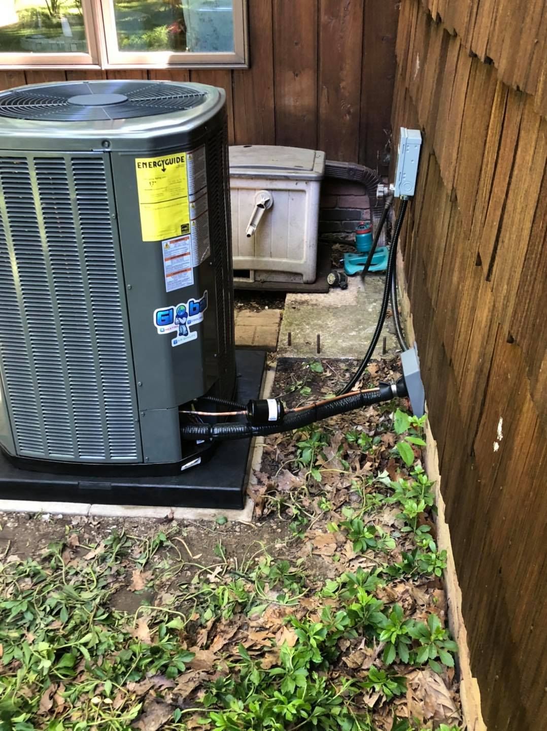 Air conditioning unit next to a wooden wall. A drain hose is connected. Green grass in foreground.