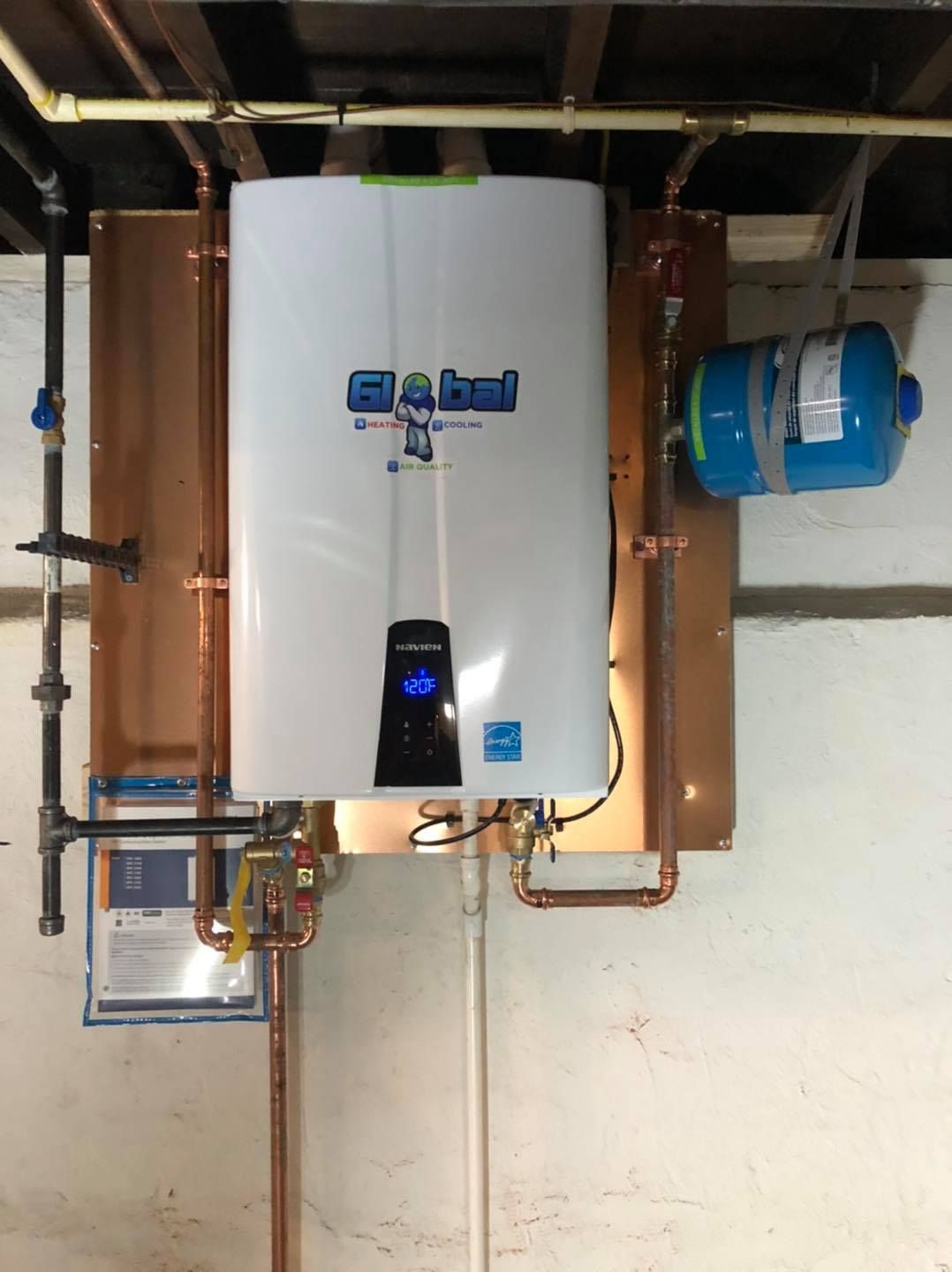 Man in blue shirt, black hat inspecting ceiling air vent, pointing to it.