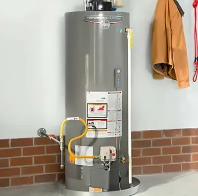 Water heater in garage, gray tank with yellow gas line and safety labels against a brick wall.