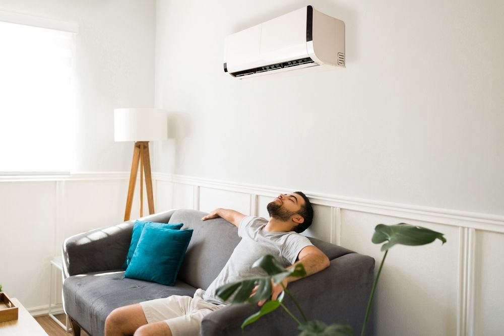 Man relaxing on a couch under an air conditioner in a bright living room.