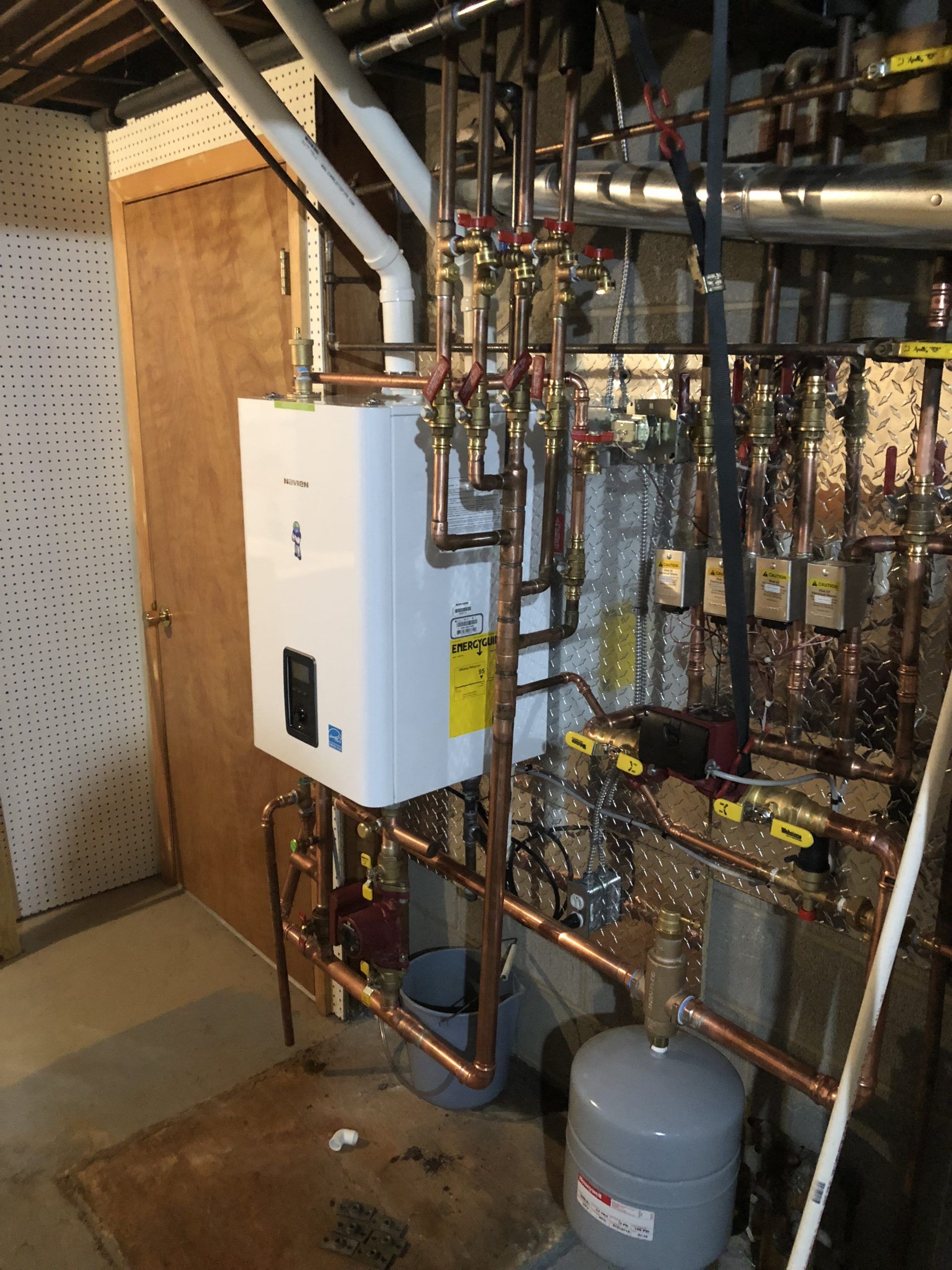 White tankless water heater with copper piping in a utility room.