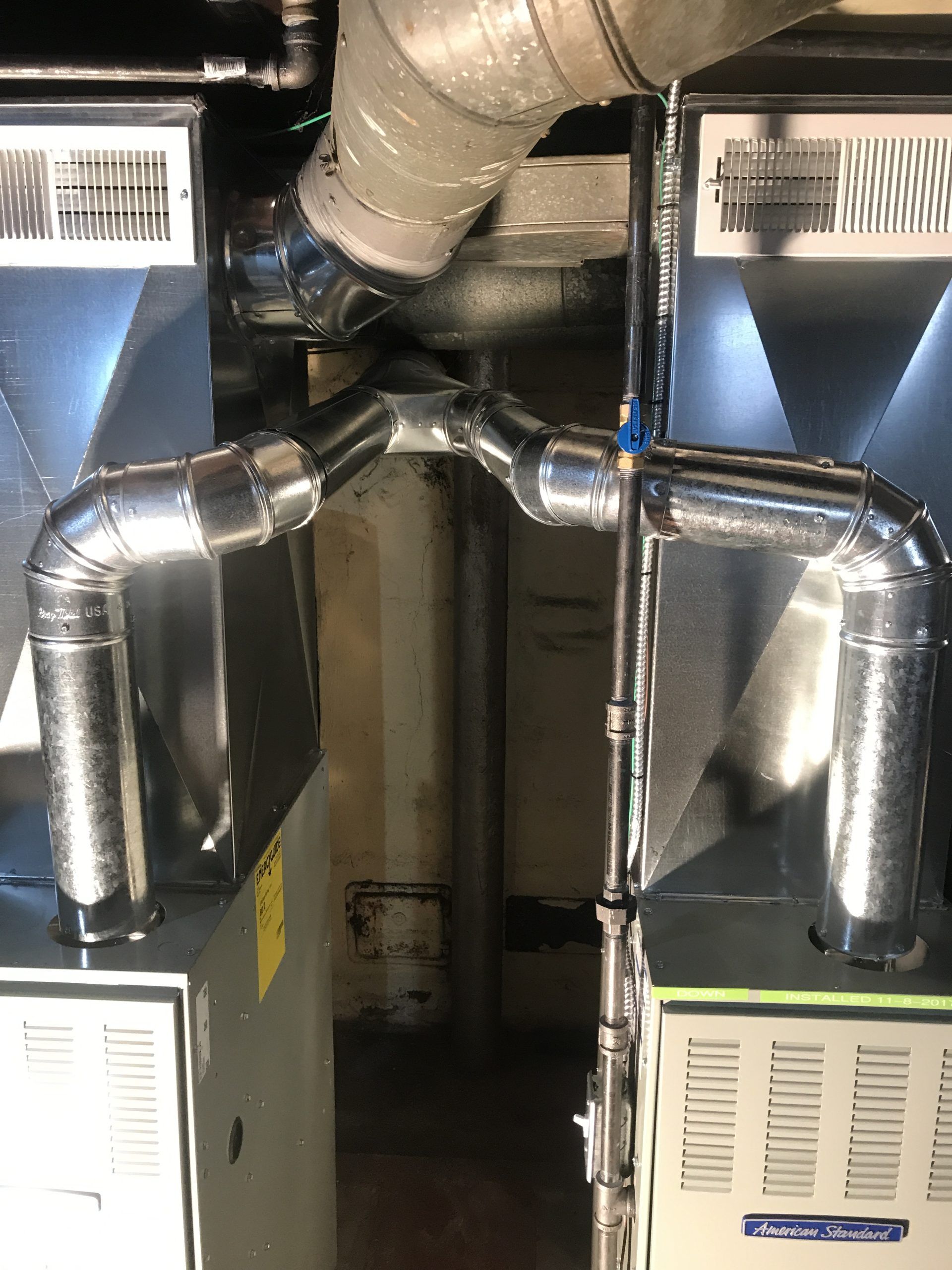 Two furnaces with connected ductwork. Metallic vents, silver pipes, and gray walls.