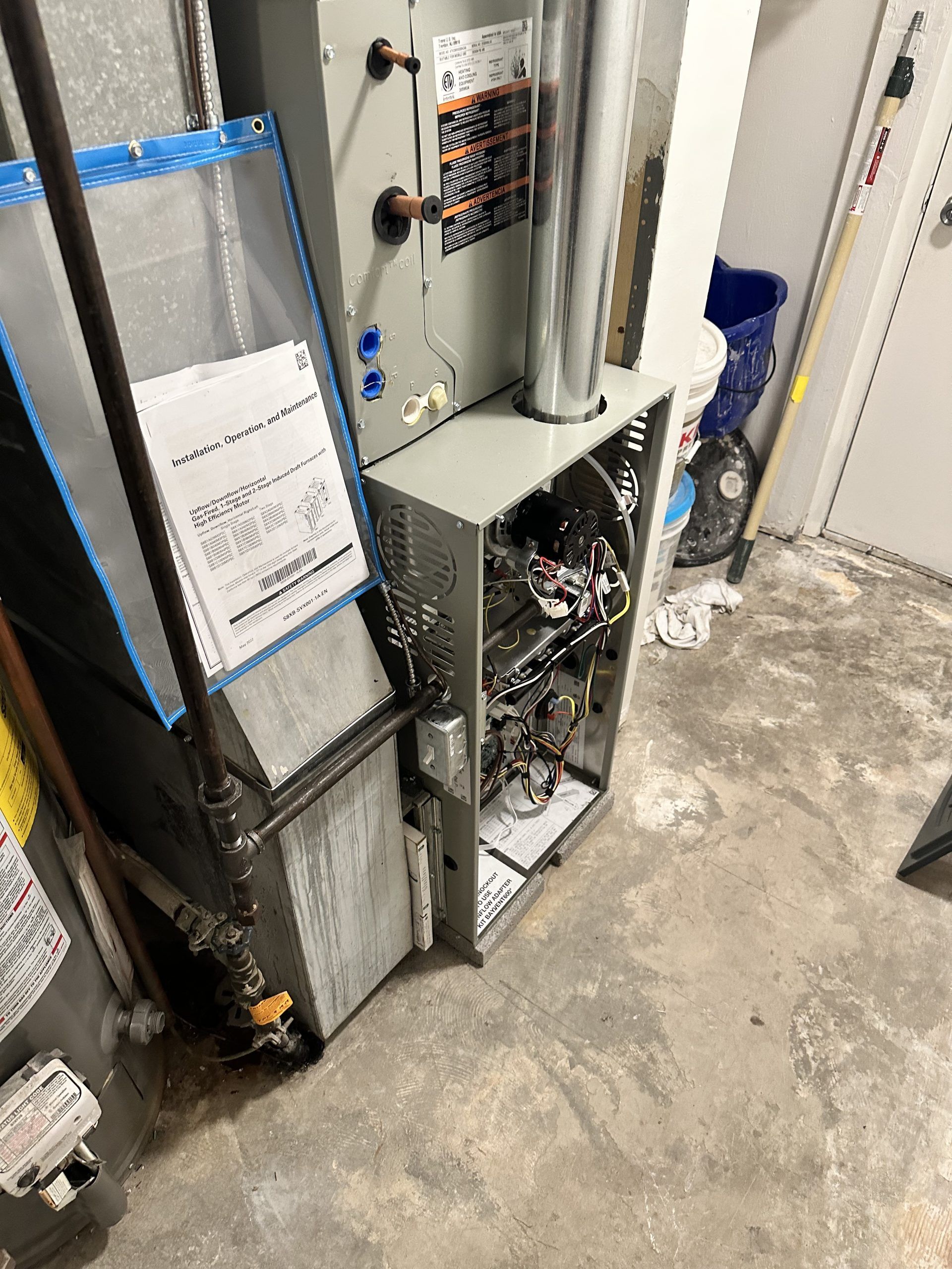 Furnace with open panels revealing internal components in a basement setting.