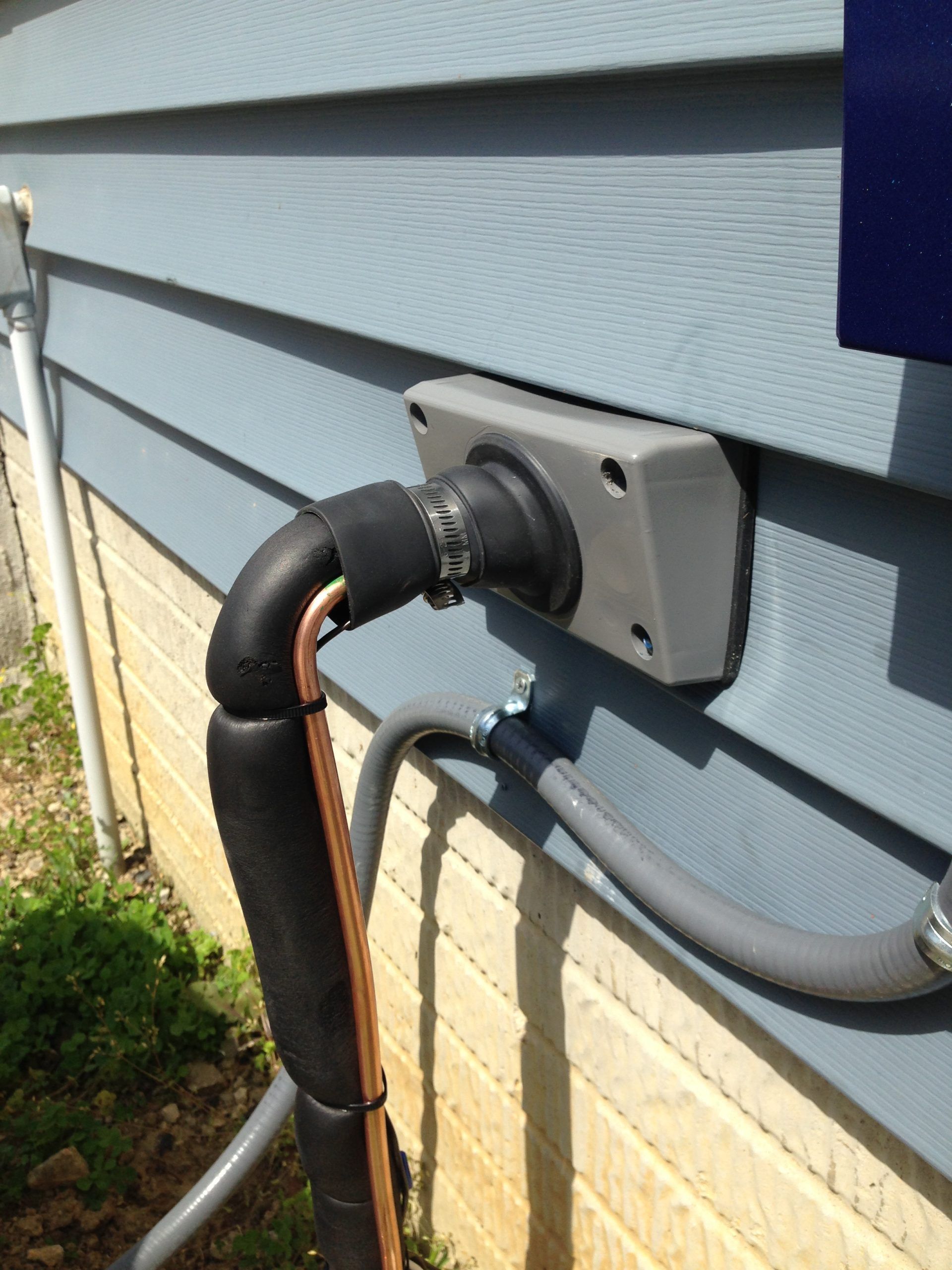 Electrical conduit and insulated copper piping exiting a house.