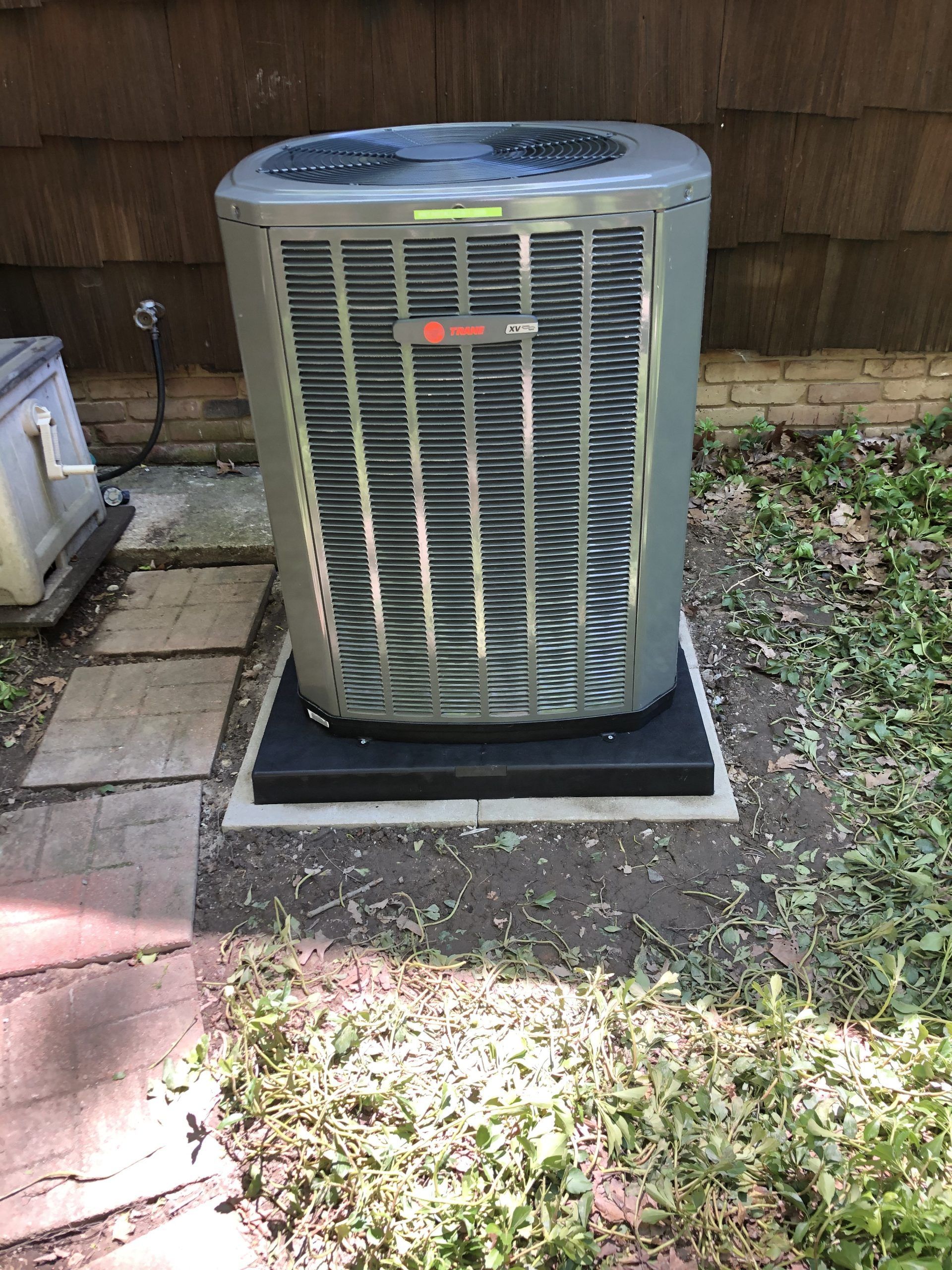 Air conditioning unit on a black base, surrounded by grass and pavers. A small hive-like structure is to the left.