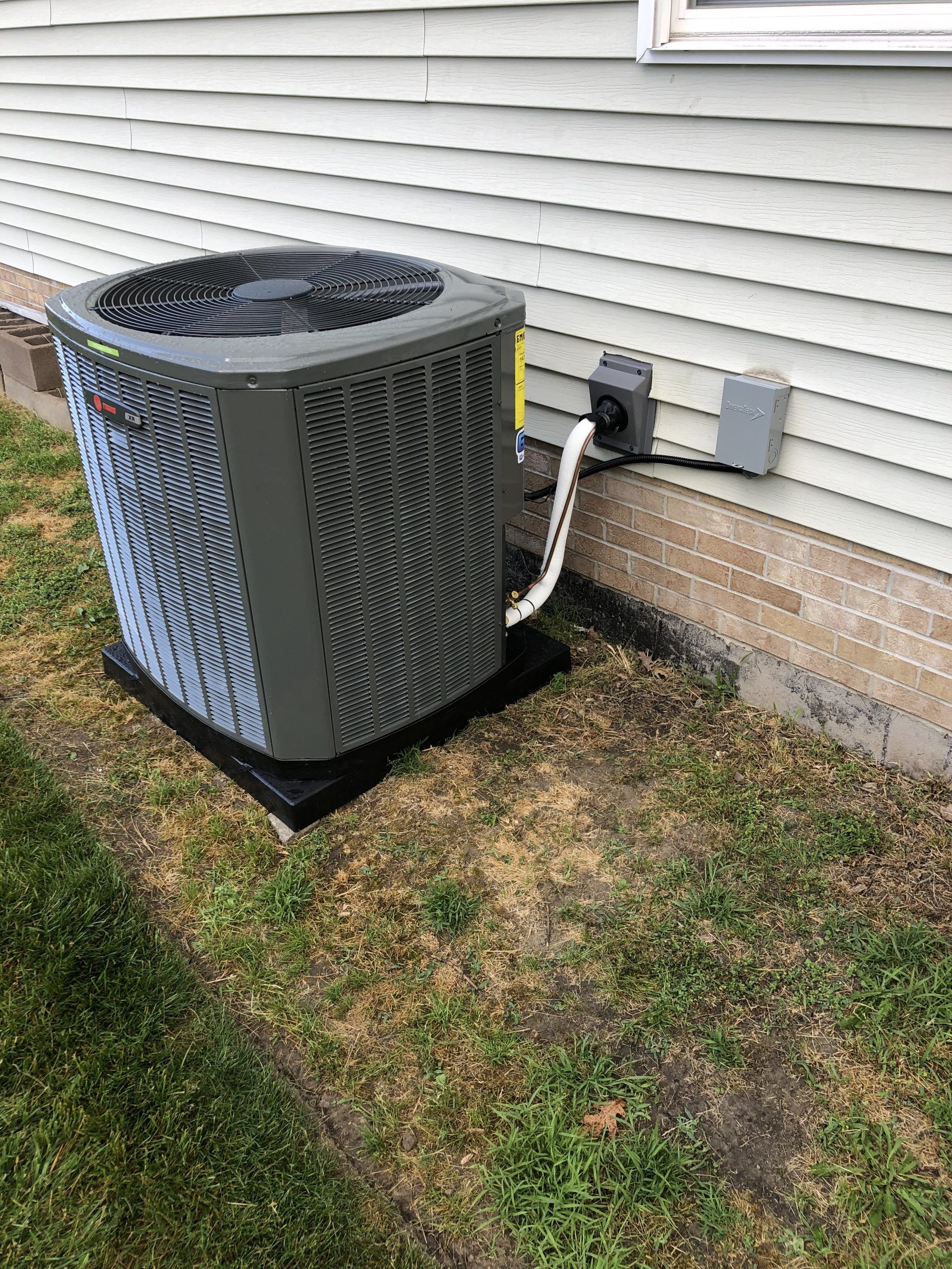 Air conditioning unit outside a light-colored house on a concrete pad, on a grassy area.