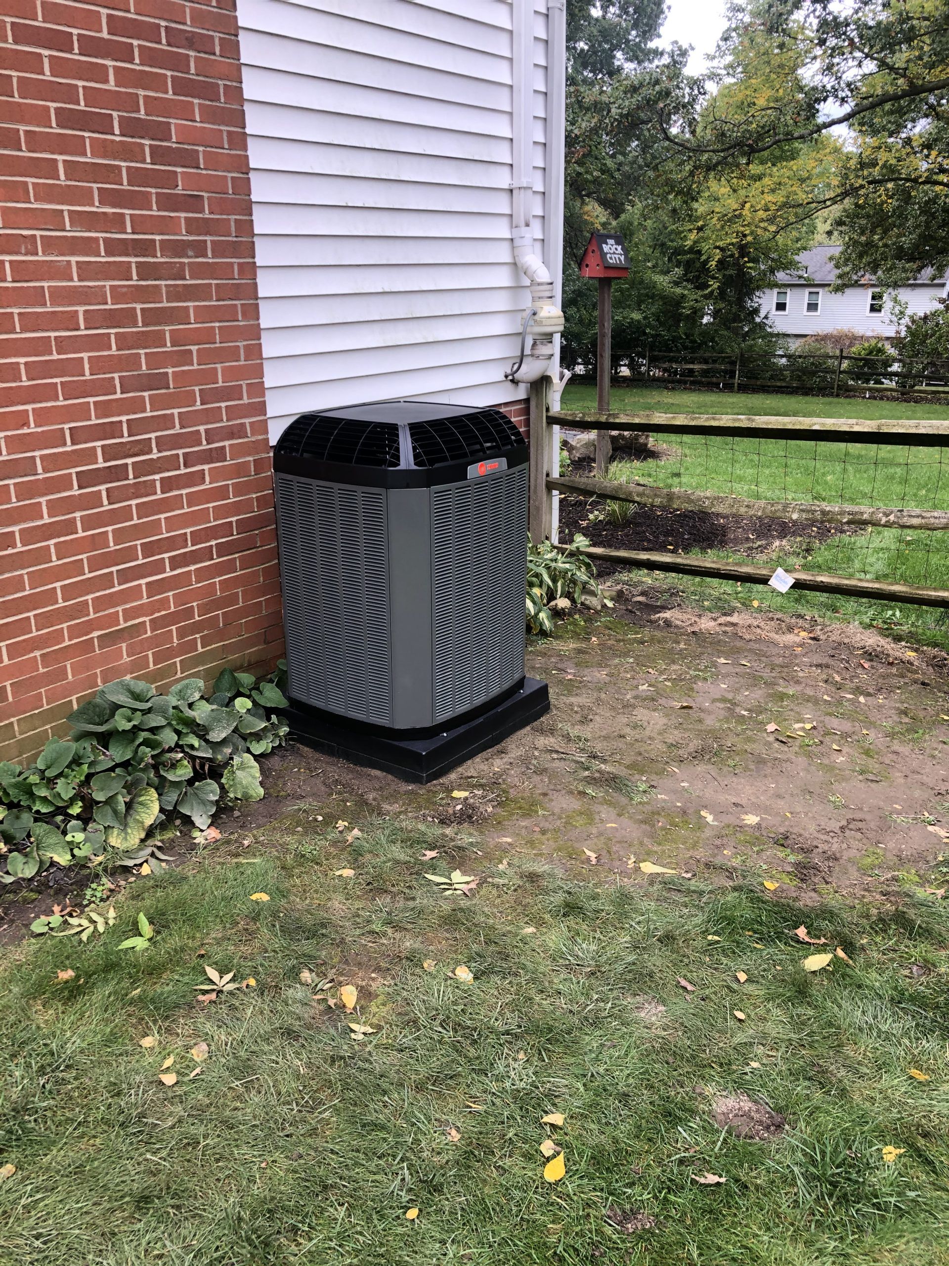 An outdoor generator next to a house with a brick wall and a wooden fence.