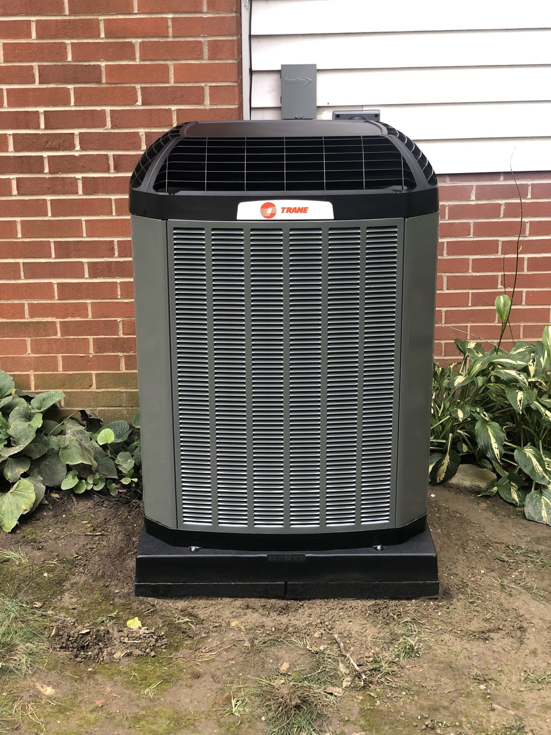 Trane air conditioning unit against a brick wall, sitting on a dark base.